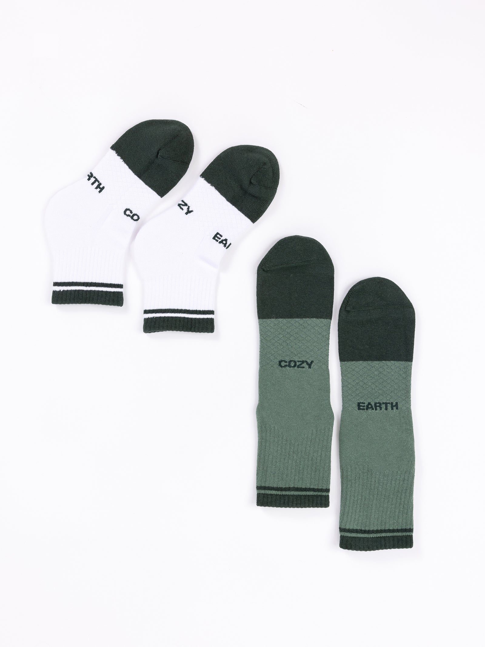 Displayed against a white backdrop are two pairs from the "Essential Quarter Sock 2-Pack" by Cozy Earth. The left pair is white with black toes and heels, featuring "COZY EARTH" on the soles. The right pair is dark green with identical writing on the soles. Both pairs come with ribbed cuffs. 