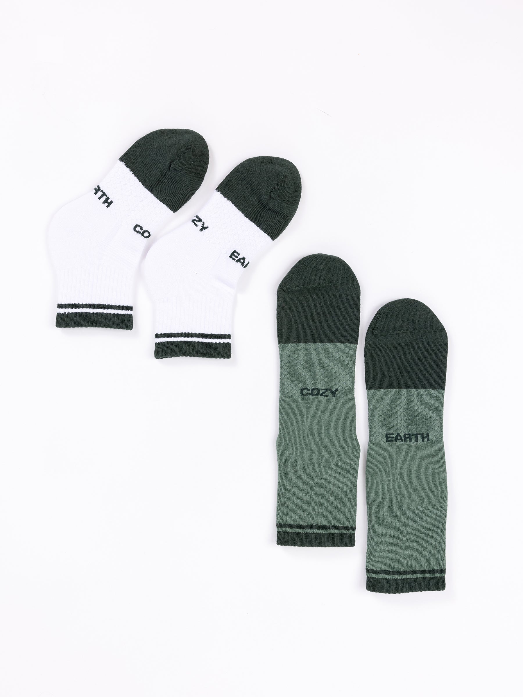 Displayed against a white backdrop are two pairs from the "Essential Quarter Sock 2-Pack" by Cozy Earth. The left pair is white with black toes and heels, featuring "COZY EARTH" on the soles. The right pair is dark green with identical writing on the soles. Both pairs come with ribbed cuffs. |Color:Spruce