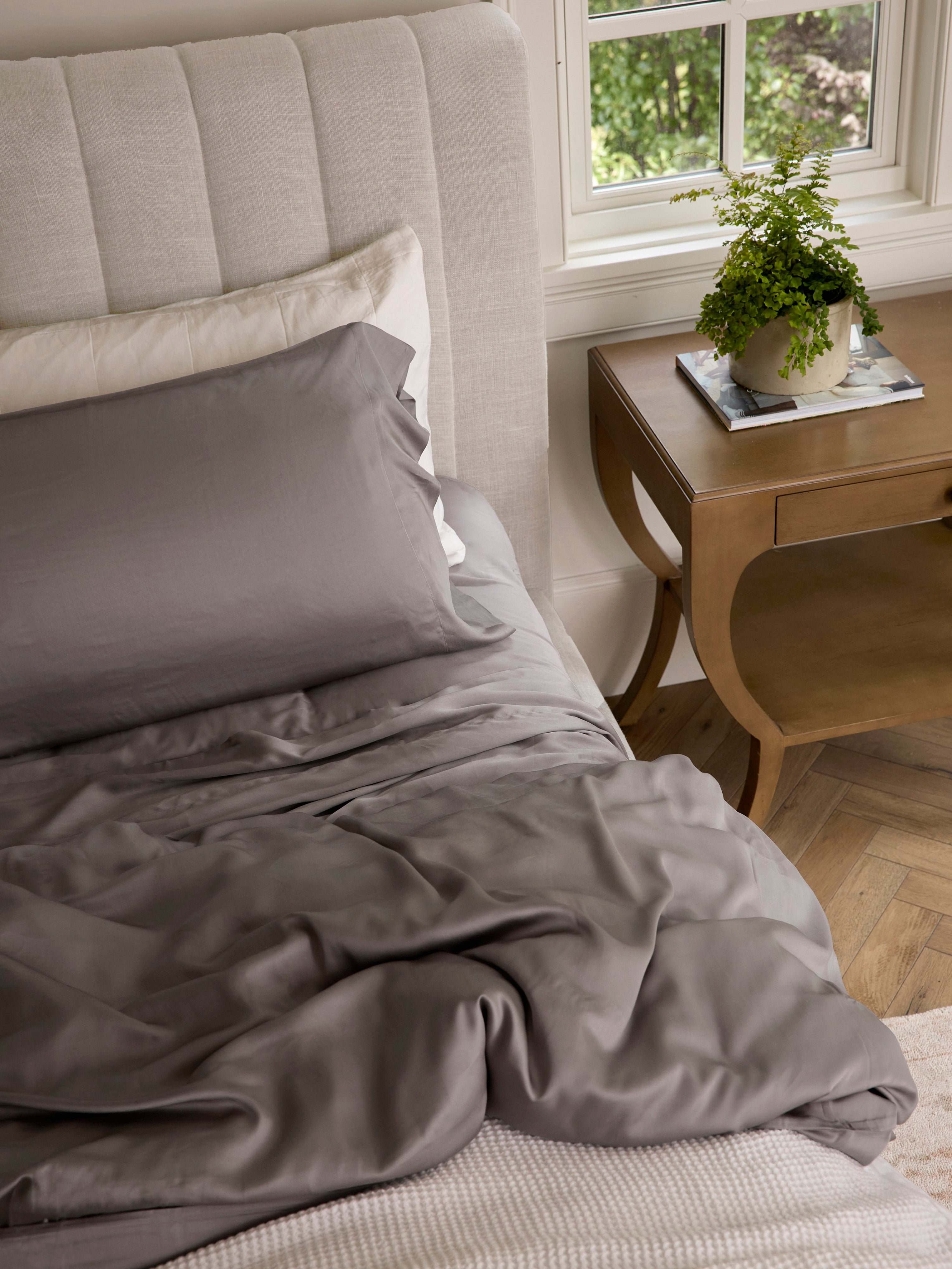 Stone bedding on an unmade bed with a plant on the nightstand |Color:Stone