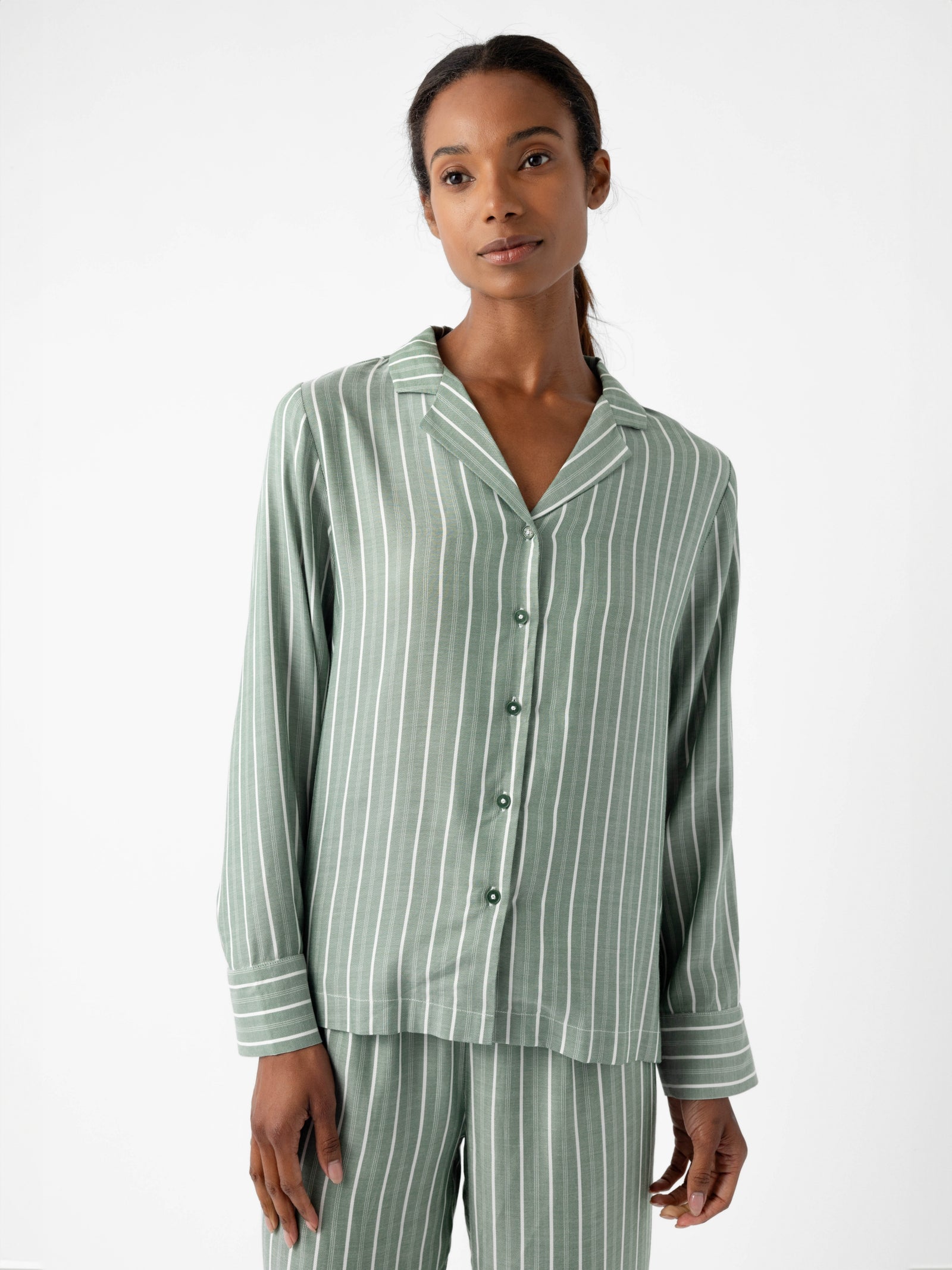 A person dressed in Cozy Earth's Women's Soft Woven Long Sleeve Pajama Top, featuring a light green and white vertical stripe design, paired with matching pants. The ensemble is set against a plain white background. 