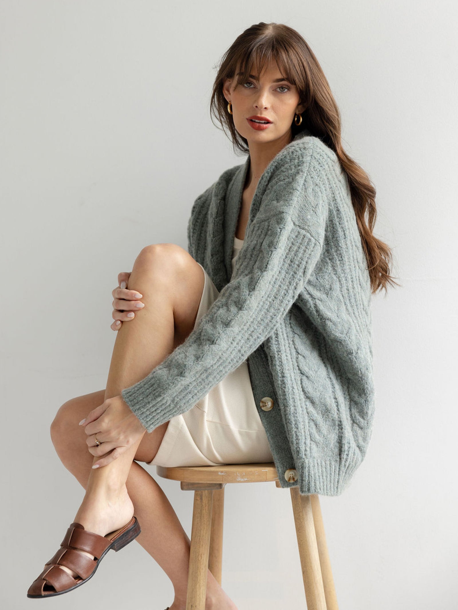 Woman sitting on wooden stool with her knee up wearing thyme cardigan 