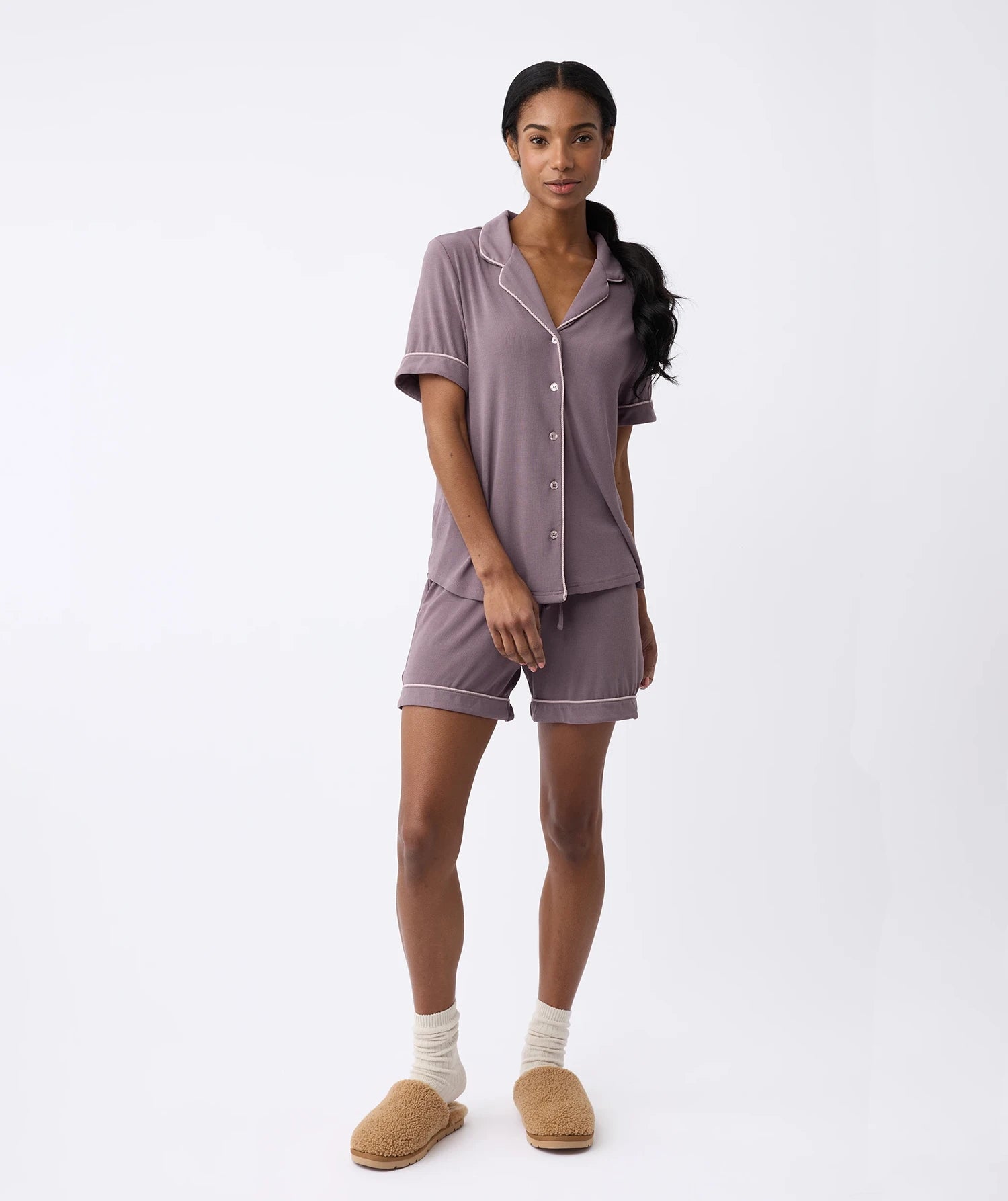 A person stands against a plain white background in the Cozy Earth Women's Bamboo Rib-Knit Classic Short Sleeve Pajama Set. They have long, dark hair pulled back and wear beige slippers with cream socks. |Color:Twilight