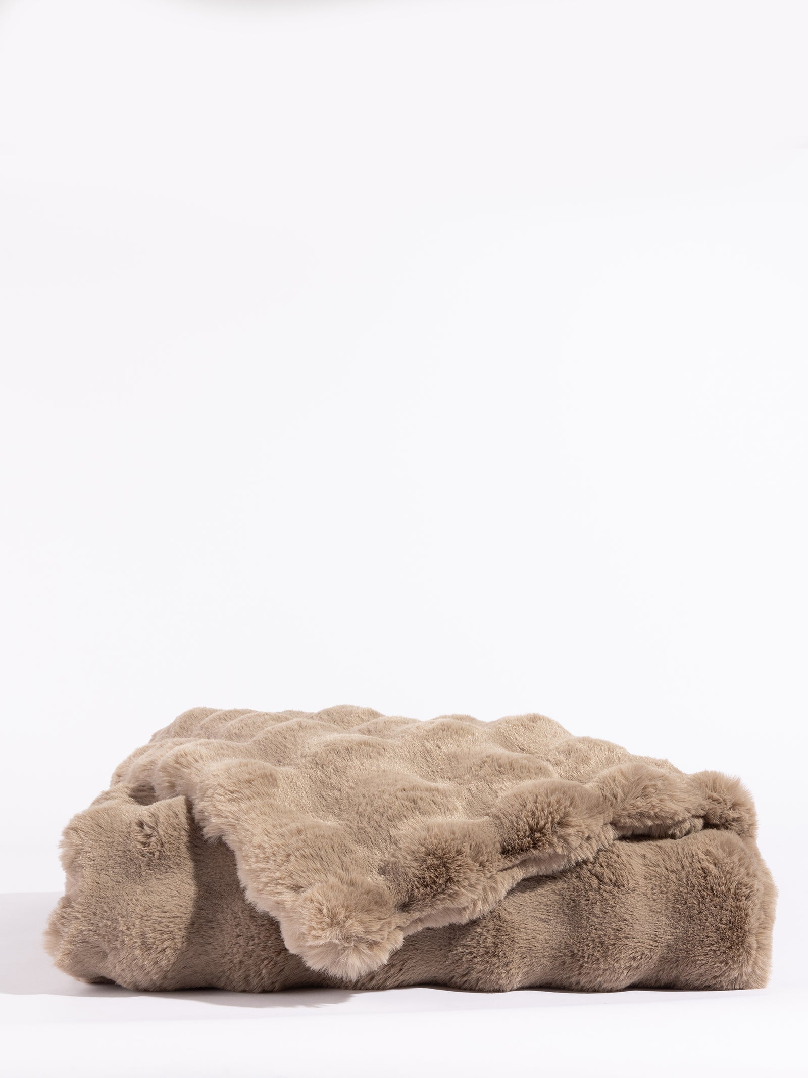 The taupe-colored Bubble Cuddle Blanket by Cozy Earth, with its soft and folded faux fur surface, sits against a white background, highlighting its plush texture. 