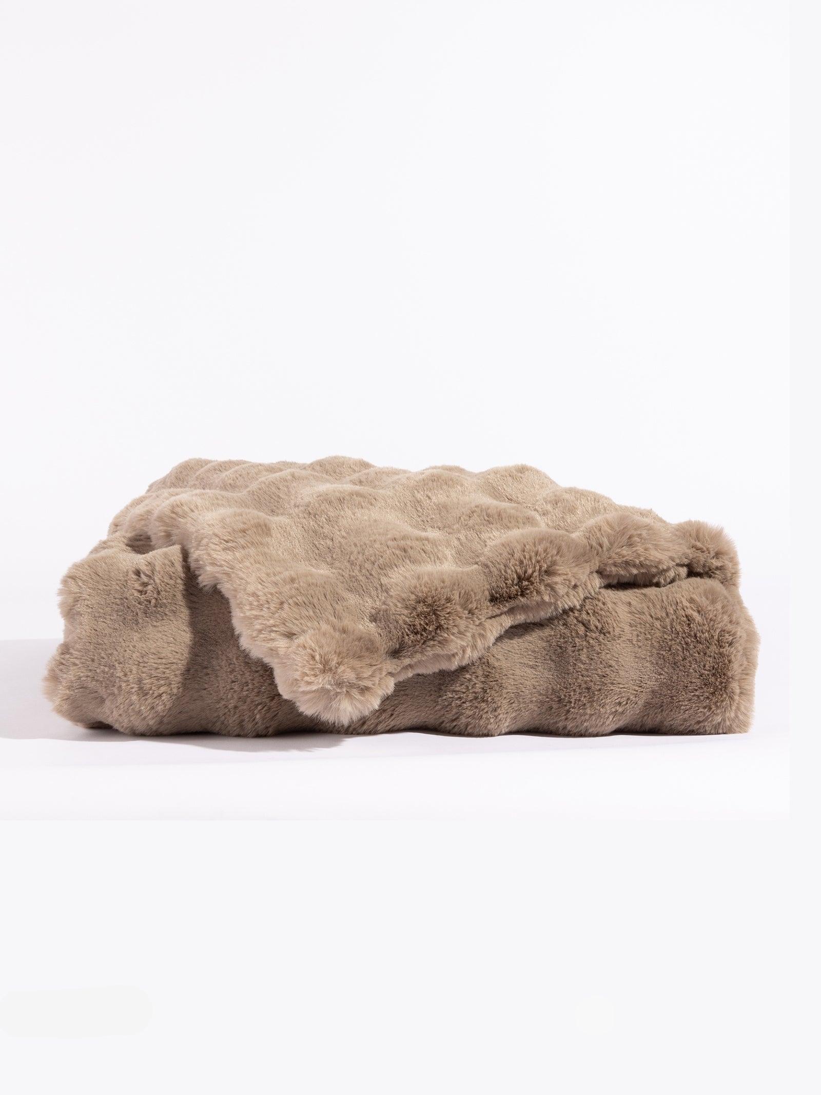 The taupe-colored Bubble Cuddle Blanket by Cozy Earth, with its soft and folded faux fur surface, sits against a white background, highlighting its plush texture. 