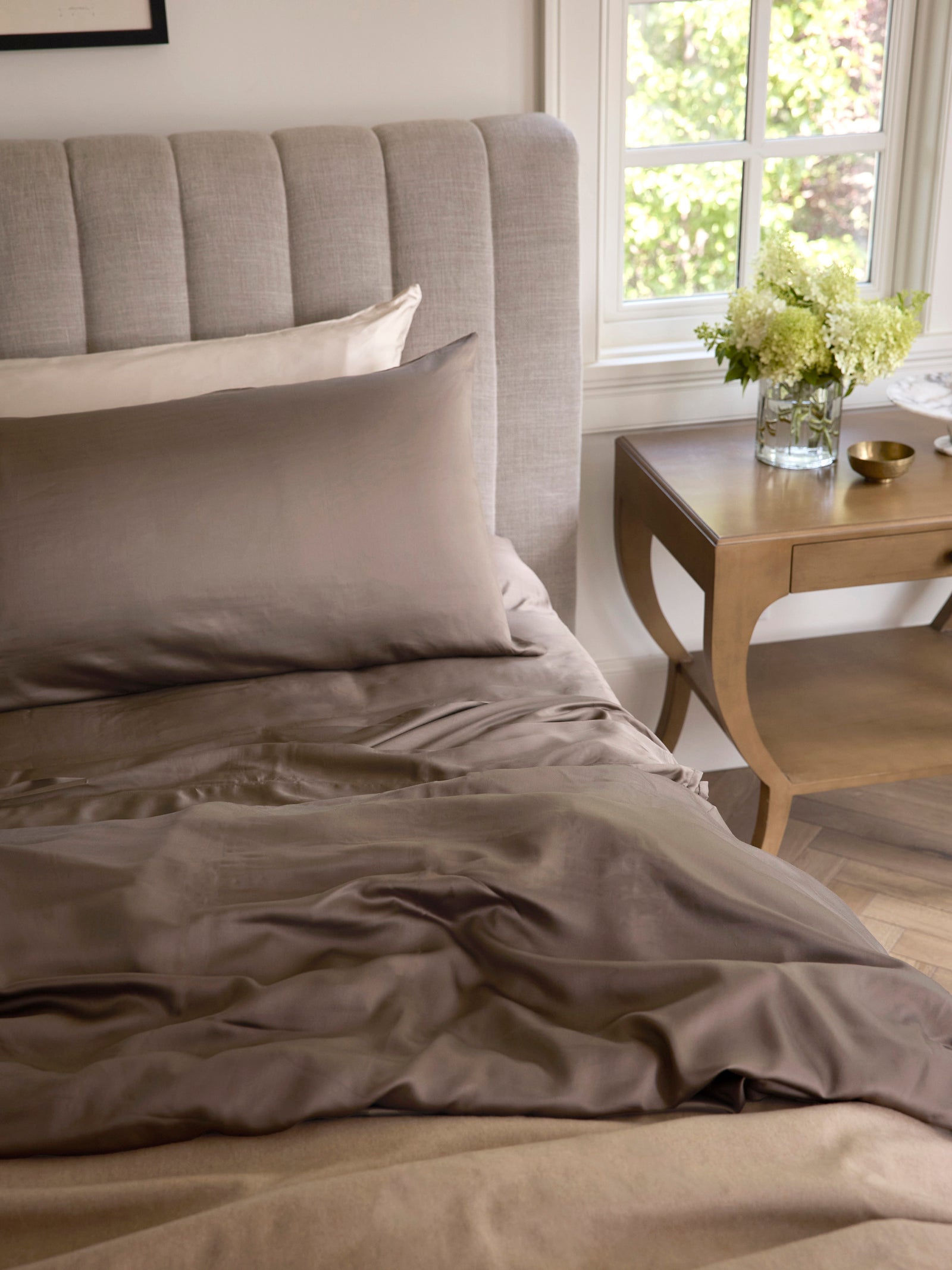 Unmade bed with walnut bedding and wooden nightstand to the side 