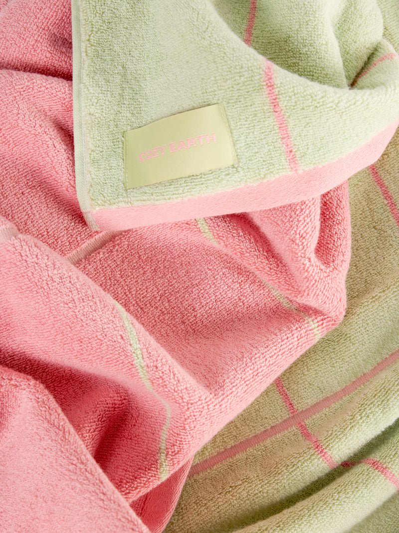 A close-up of a soft, folded towel with a pink and green plaid pattern. A label on the towel reads "Cozy Earth." The fabric's textures are clearly visible, highlighting its softness. 