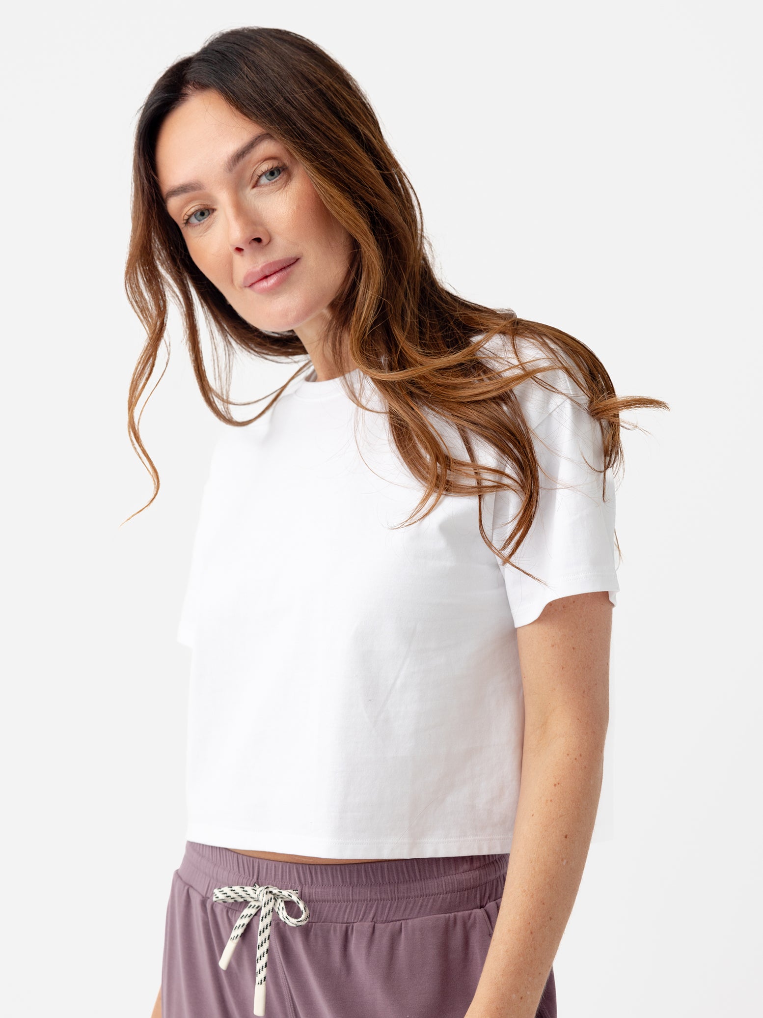 White All Day Cropped Tee. The photo of the All Day Cropped Tee is taken with a with a white background and is worn by a woman. 