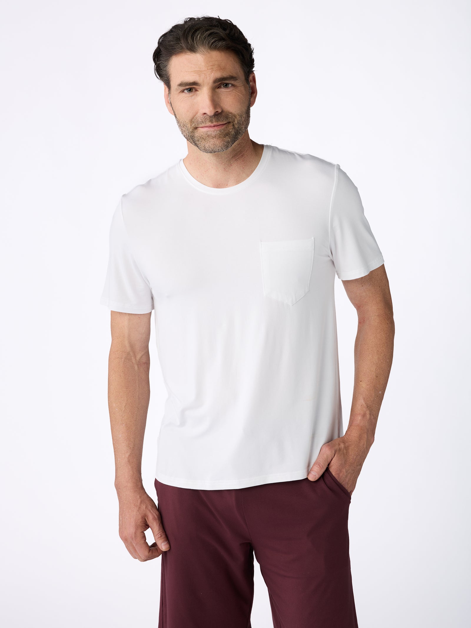 A man with short dark hair and a beard is wearing the Men's Stretch-Knit Bamboo Lounge Tee by Cozy Earth, paired with maroon pants. He is standing against a plain white background, looking at the camera with a relaxed expression. 