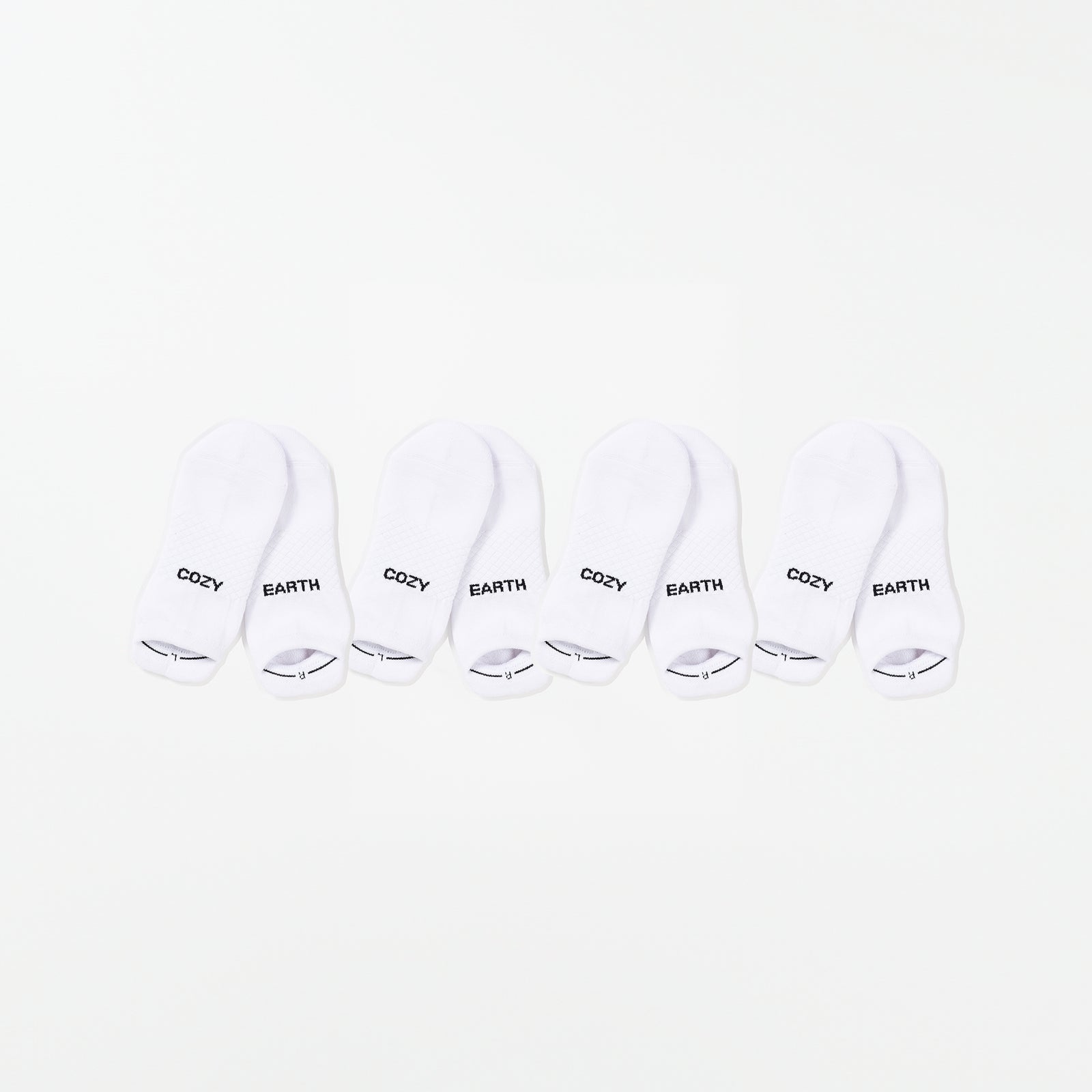 Four pairs of white ankle socks from the Essential Ankle Sock 4-Pack by Cozy Earth are arranged in a row against a white background. The words "COZY" and "EARTH" are printed on the socks' toes in black text. 