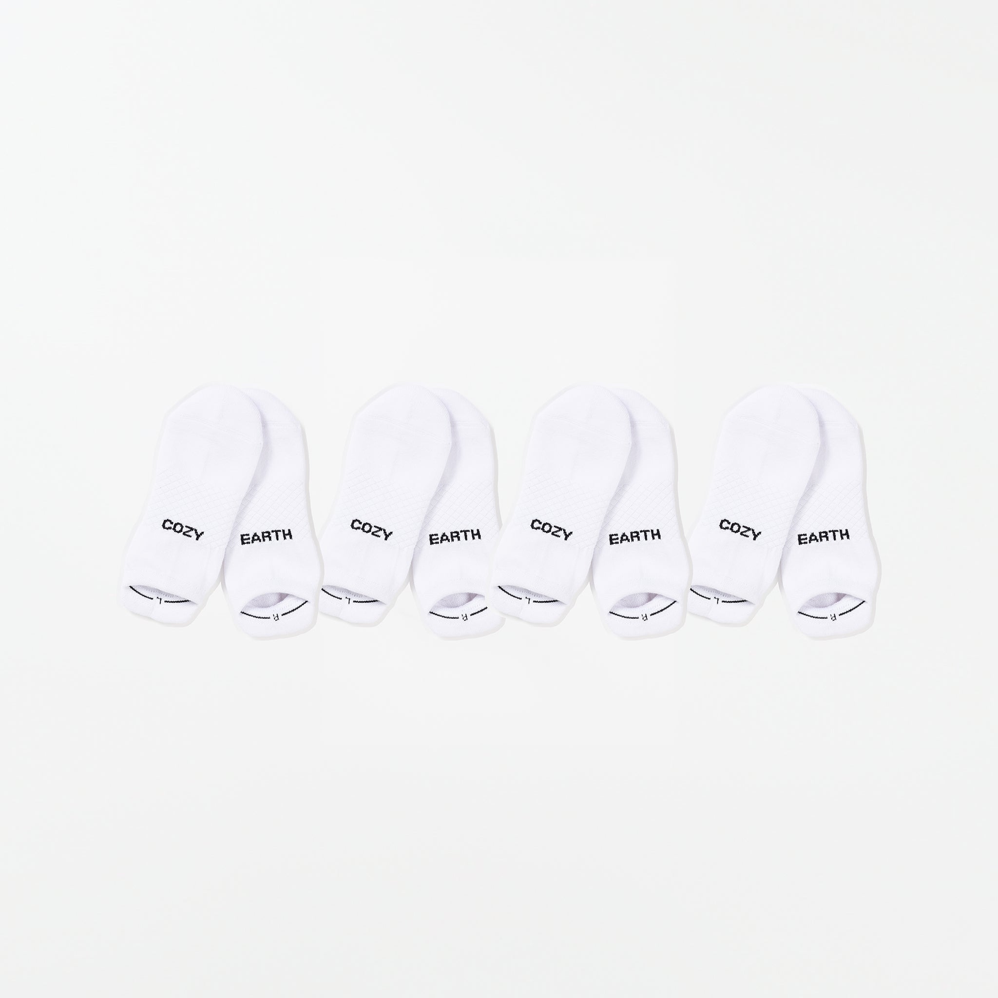 Four pairs of white ankle socks from the Essential Ankle Sock 4-Pack by Cozy Earth are arranged in a row against a white background. The words "COZY" and "EARTH" are printed on the socks' toes in black text. |Color:White