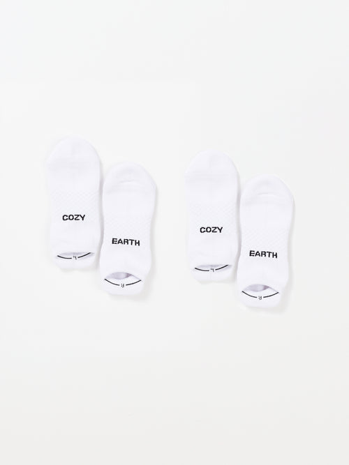 Two pairs of white Essential Ankle Socks from Cozy Earth are laid out on a plain background. The socks on the left have 