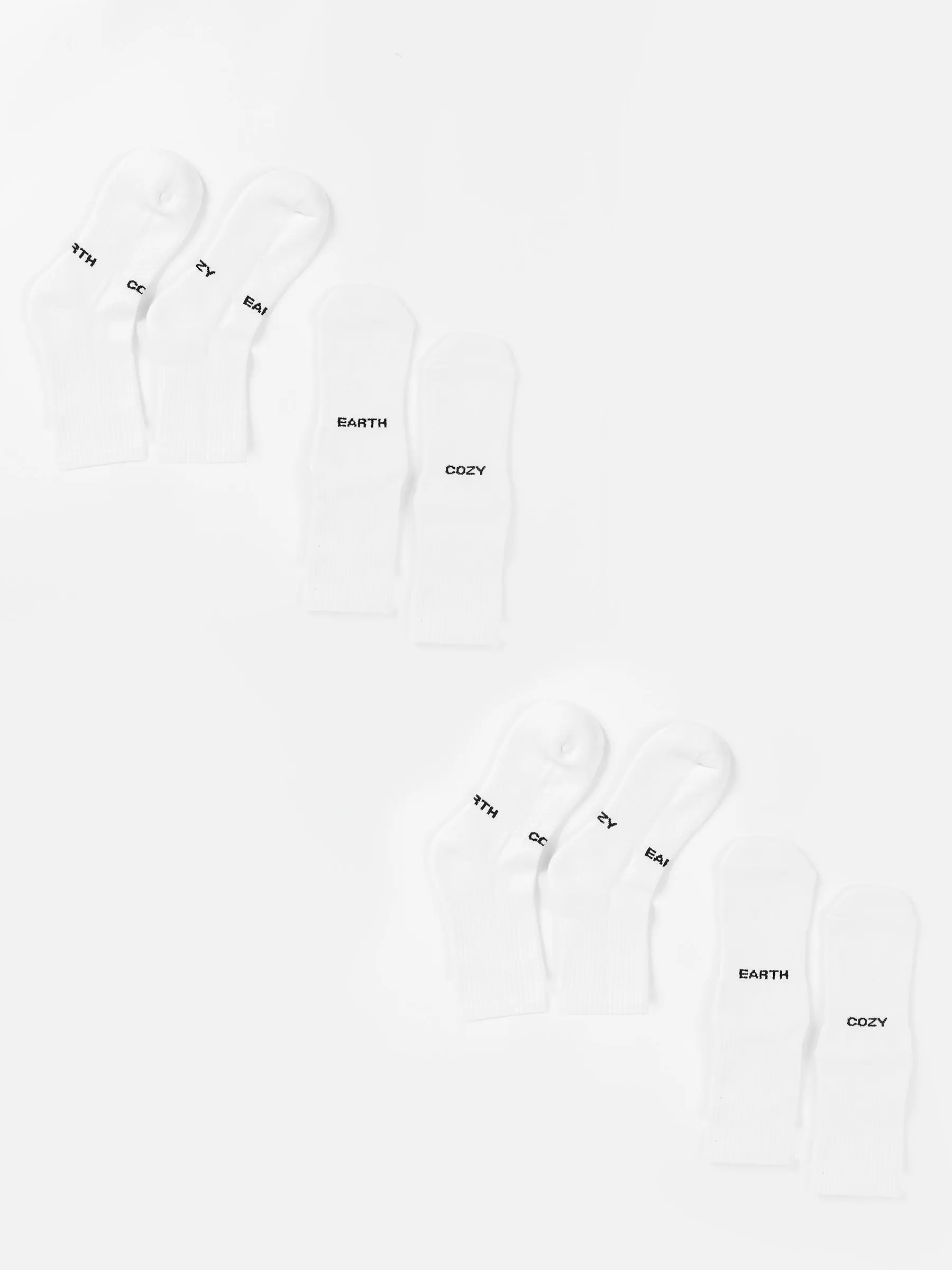 Two sets of three pairs of white Essential Calf Sock 4-Packs from Cozy Earth are arranged in two rows on a white background. Each sock is labeled with the words "MYTH," "EARTH," or "COZY" in black text near the toes. The arrangement is neat, with one set of socks mirroring the other. |Color:White