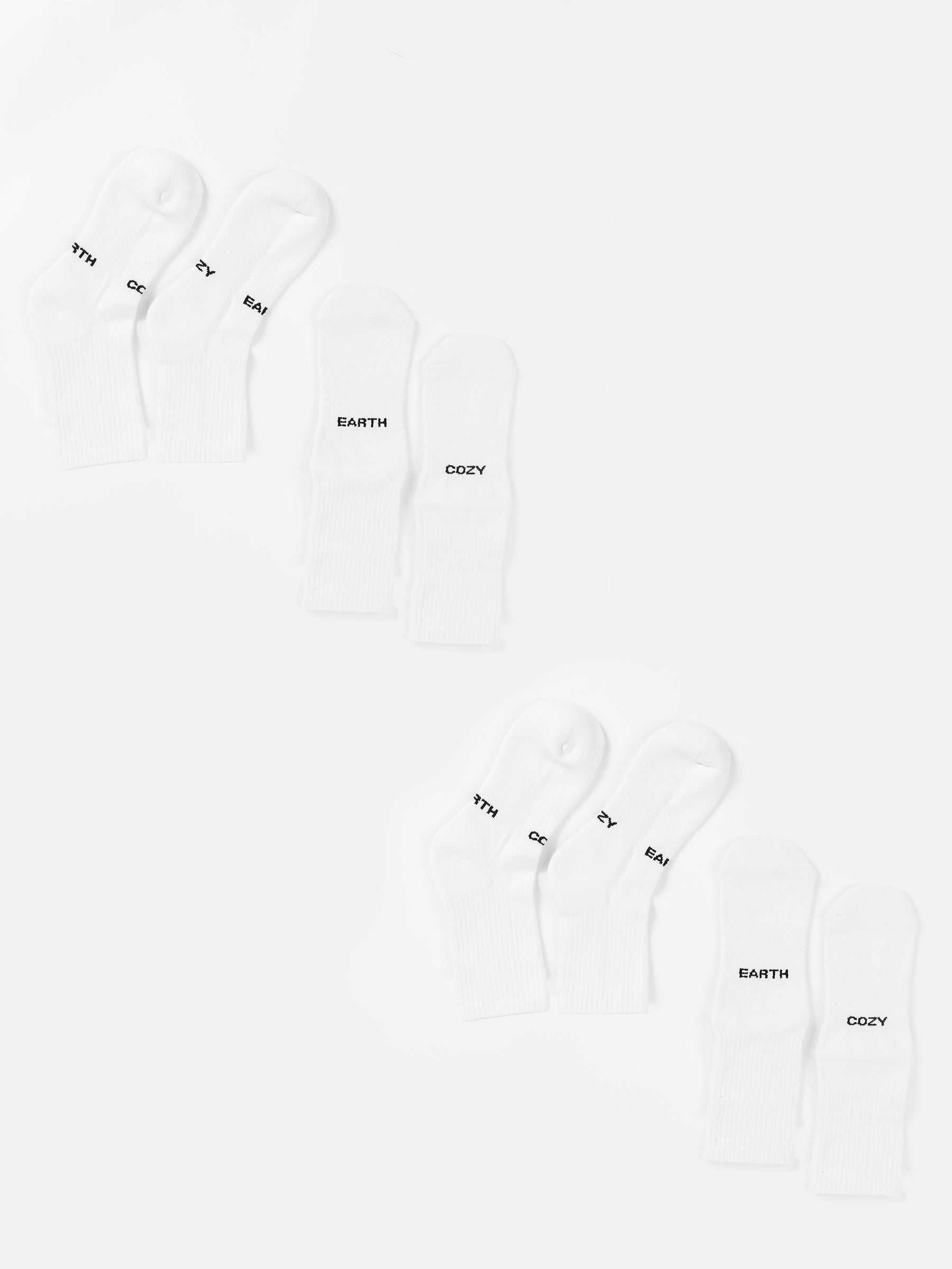 Two sets of three pairs of white Essential Calf Sock 4-Packs from Cozy Earth are arranged in two rows on a white background. Each sock is labeled with the words "MYTH," "EARTH," or "COZY" in black text near the toes. The arrangement is neat, with one set of socks mirroring the other. |Color:White