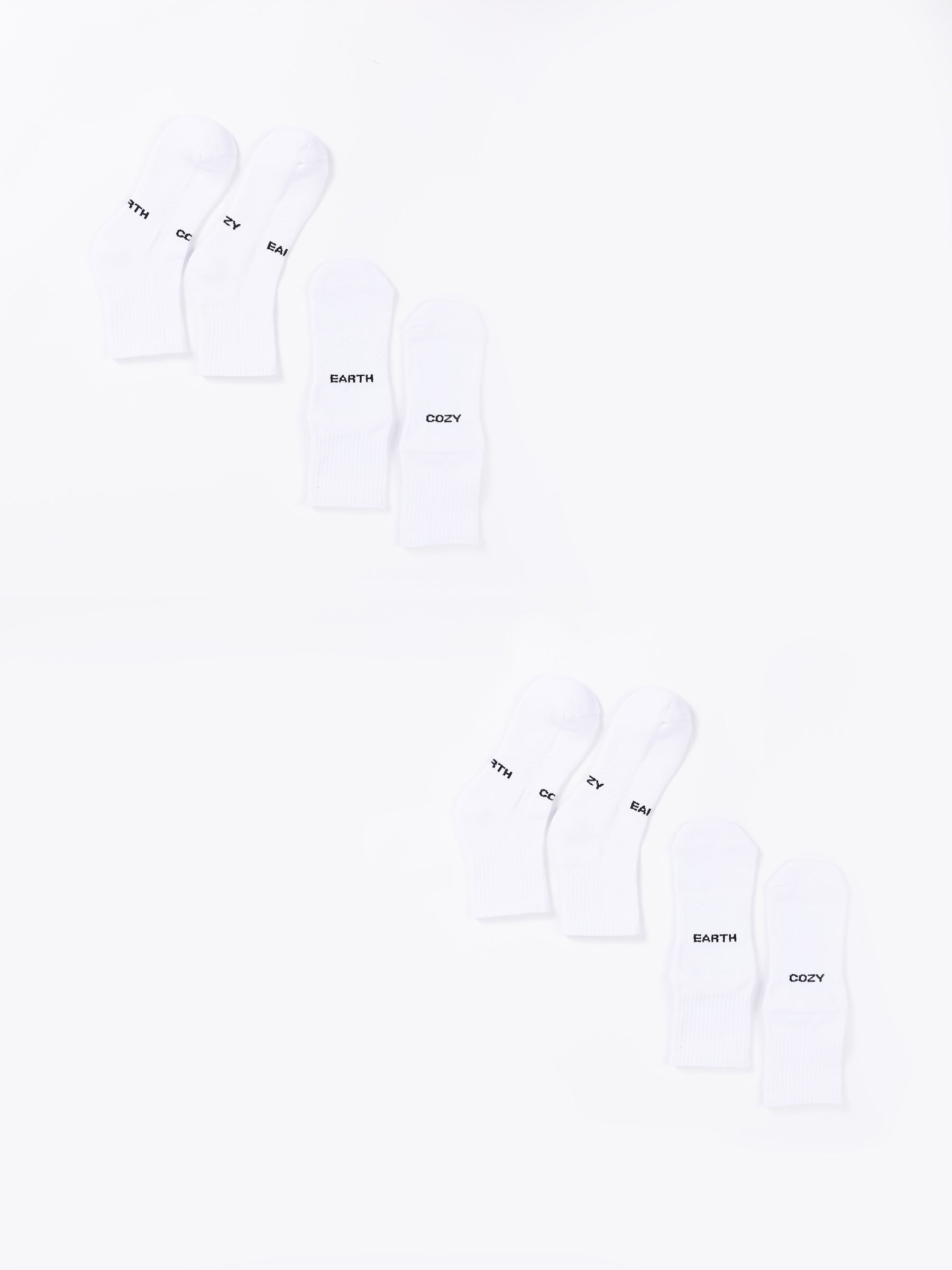 The Essential Quarter Sock 4-Pack from Cozy Earth includes eight white socks arranged in two rows, with each row containing four pairs. The socks feature various words printed on them, such as "EARTH," "COZY," and "THY." The plain white background provides a clean and minimalist appearance. 
