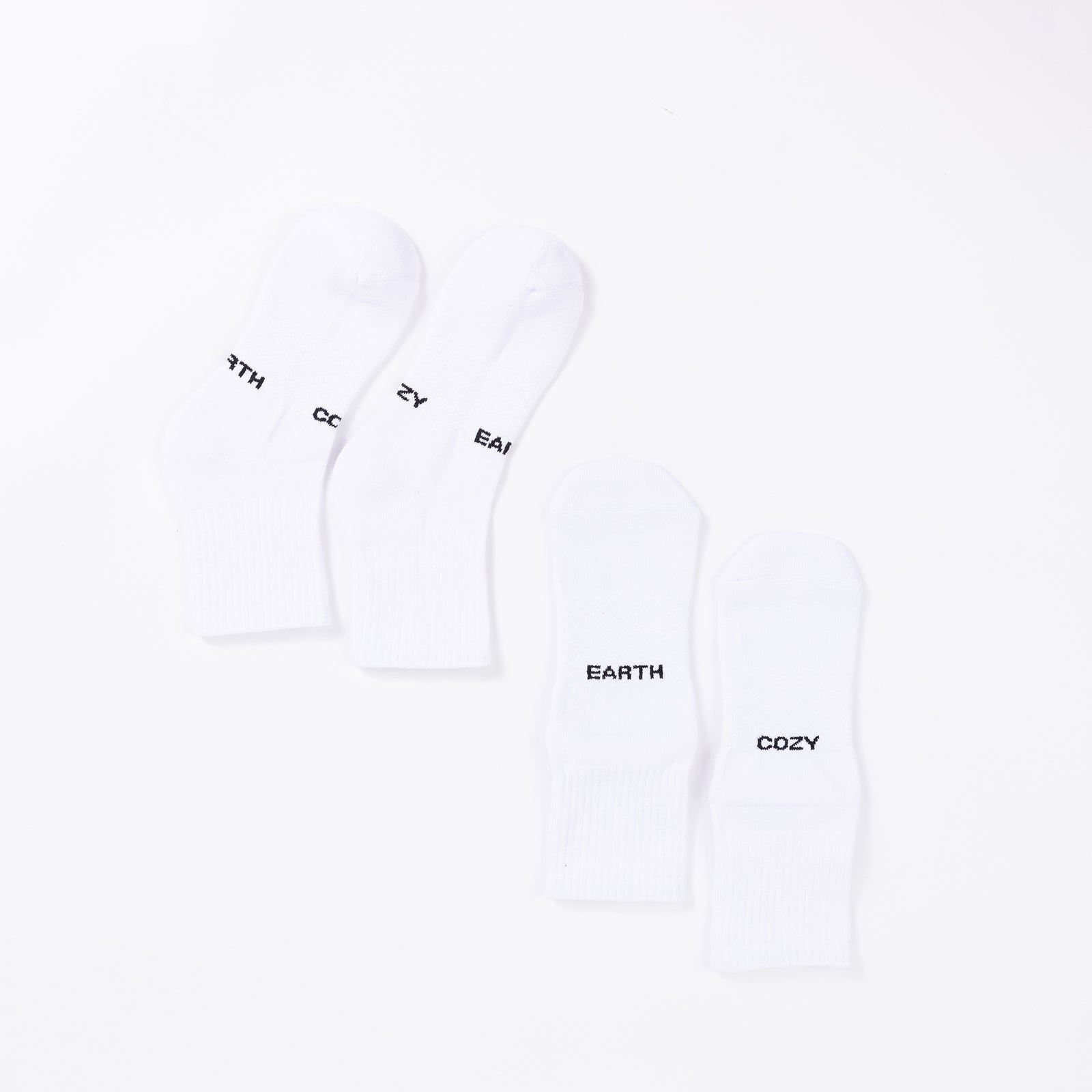 A pair of white Essential Quarter Socks from Cozy Earth is positioned vertically on the left, with the words "EARTH" and "COZY" displayed in black text on each sock. Another similar pair is positioned to the right. The socks are placed against a plain white background. 