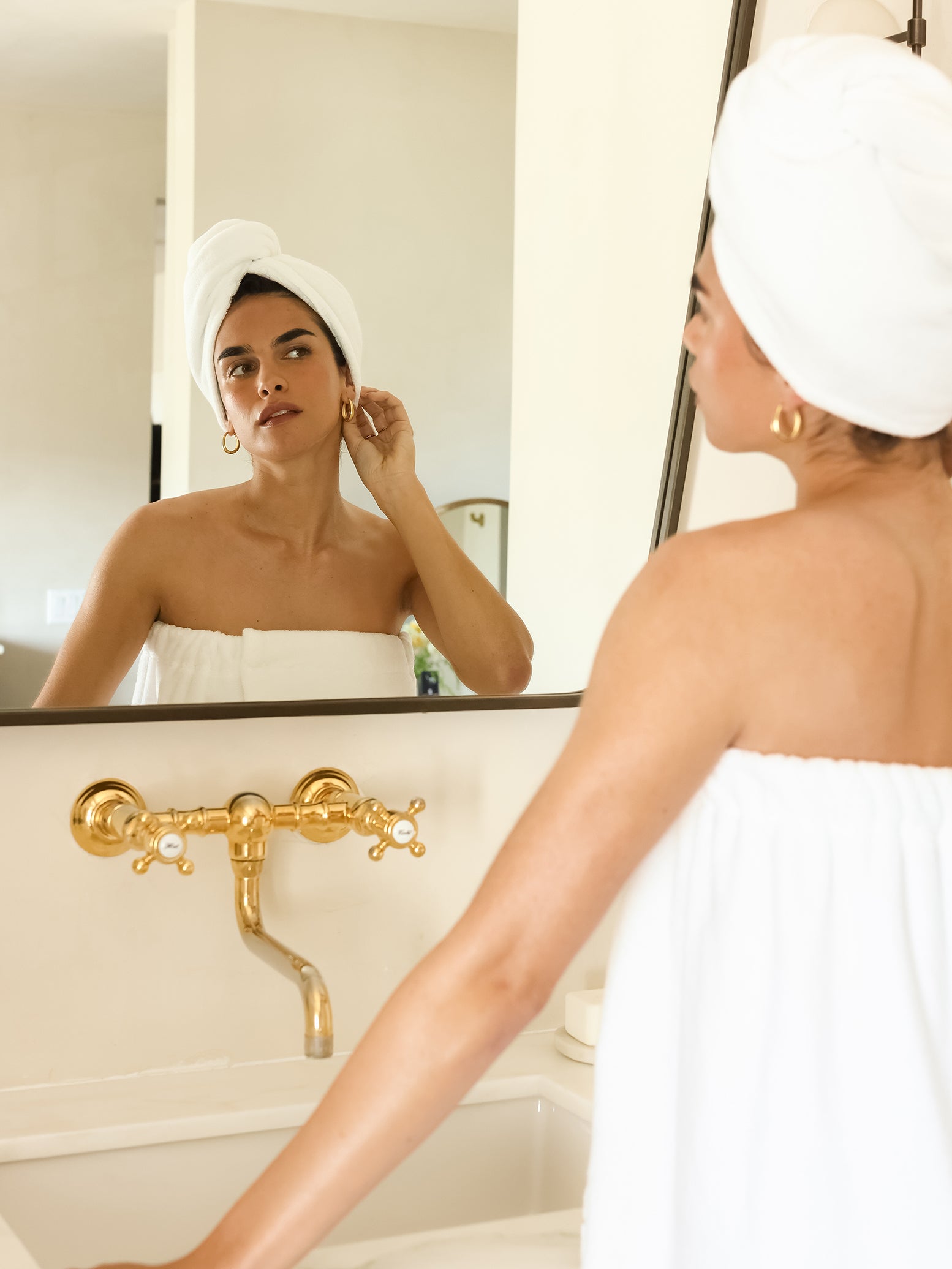Woman with white hair towel looking in bathroom mirror 