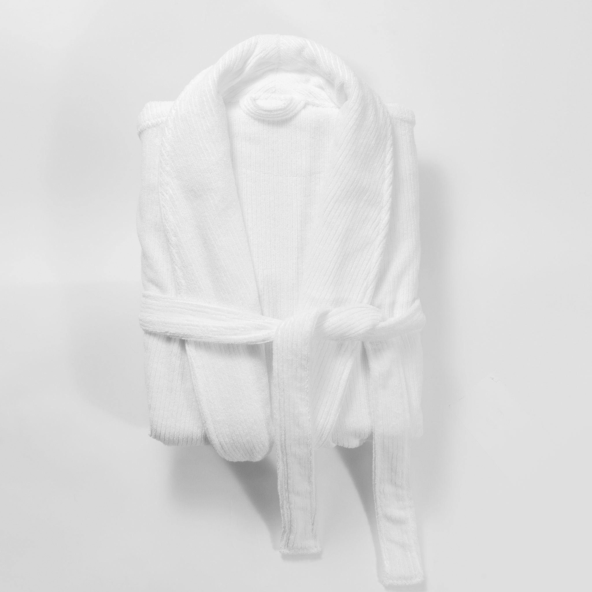 A Cozy Earth Ribbed Terry Bath Robe, in white and plush material, is neatly folded with its belt tied at the front and placed against a plain white background. 