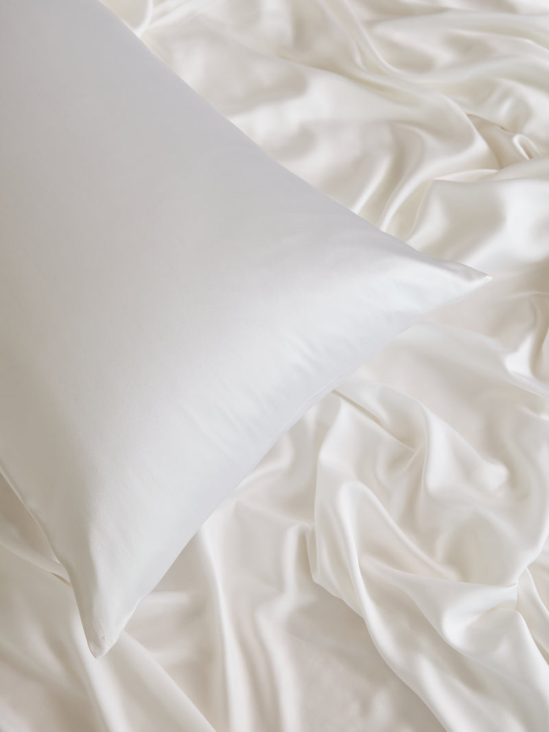 A Cozy Earth Silk Pillowcase rests on a bed adorned with a matching silk sheet. The fabric's smooth and shiny appearance exudes a luxurious and inviting texture.
