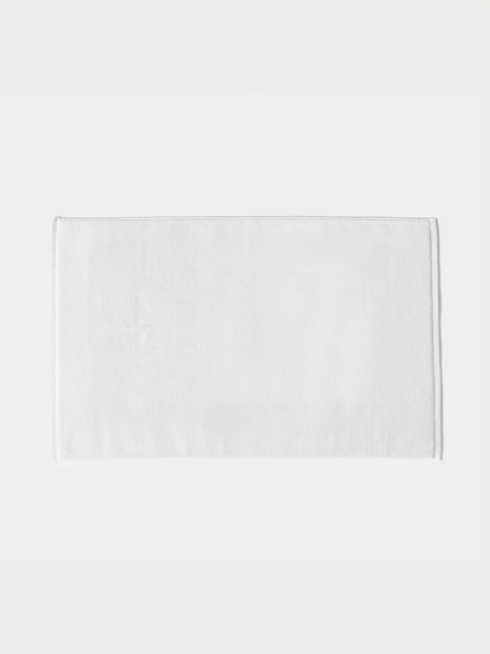 White looped terry bath mat resting on white background.