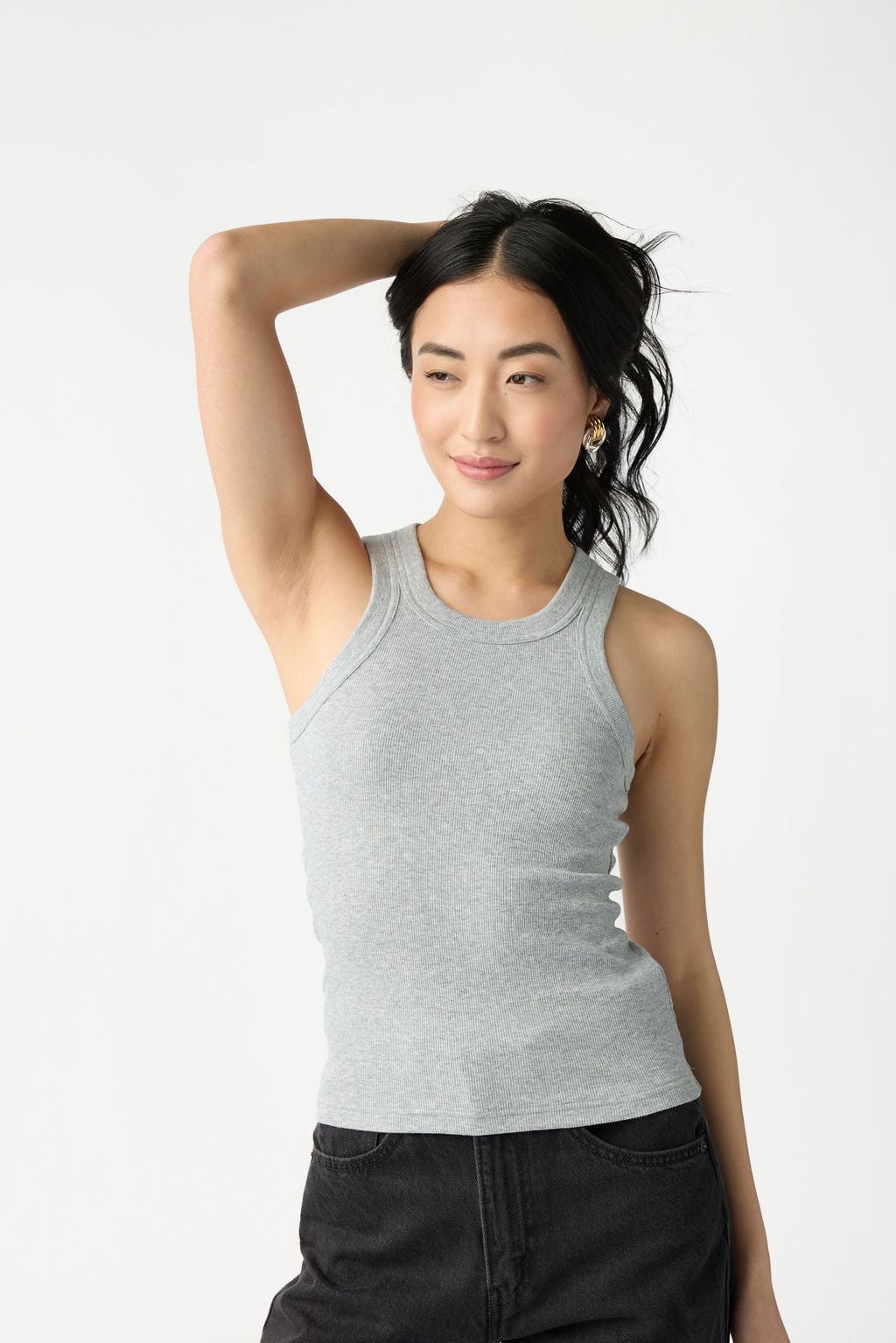 A dark haired woman wears Cozy Earth Women's Fine Ribbed Tank in Heather Grey. She holds her hair up with one hand and stands in front of a white background. |Color:Heather Grey