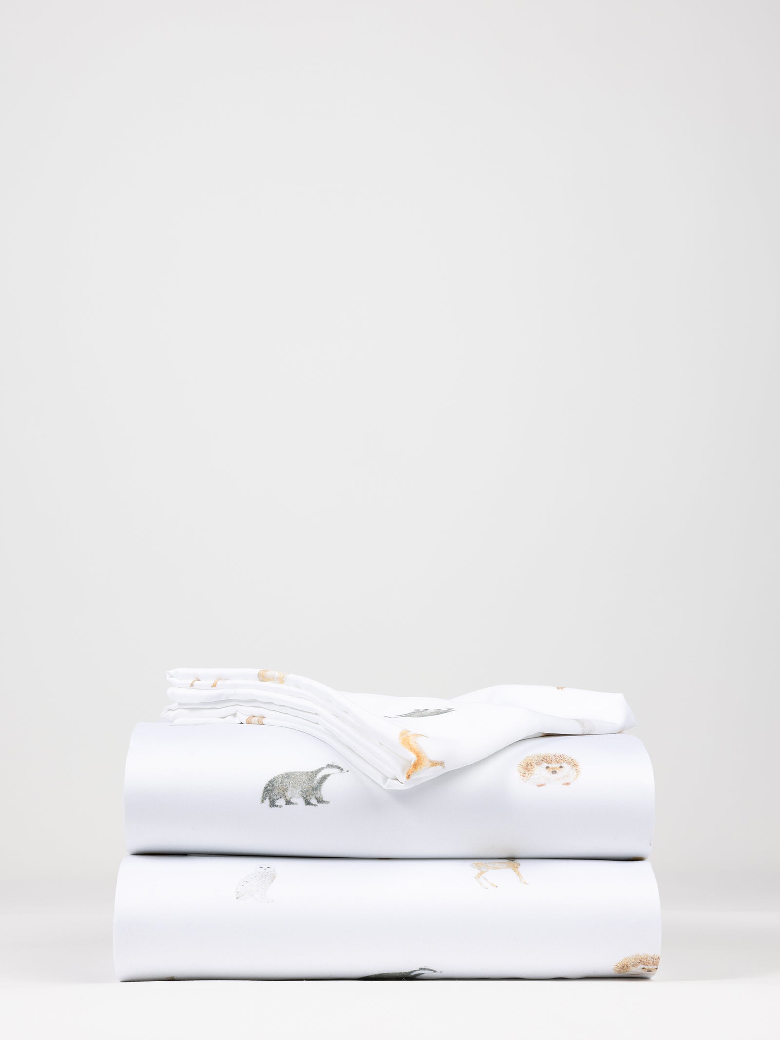 A neatly stacked set of the Bamboo Sheet Set by Cozy Earth, featuring subtle illustrations of bears and other creatures. The sheets are white, providing a clean backdrop for the playful designs. 