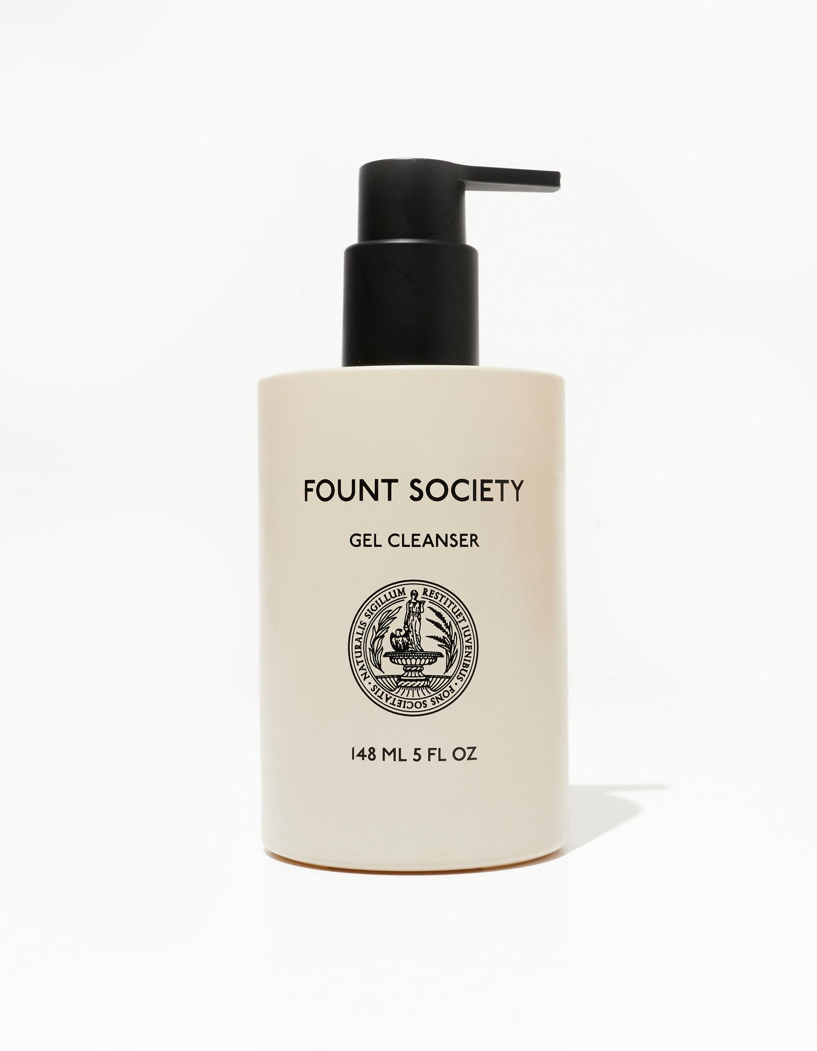 Beige bottle of Day-to-Night Essentials features a black pump. The text includes "GEL CLEANSER" and "148 ML 5 FL OZ," accompanied by a circular logo with a fountain and surrounding text, from the brand Cozy Earth.