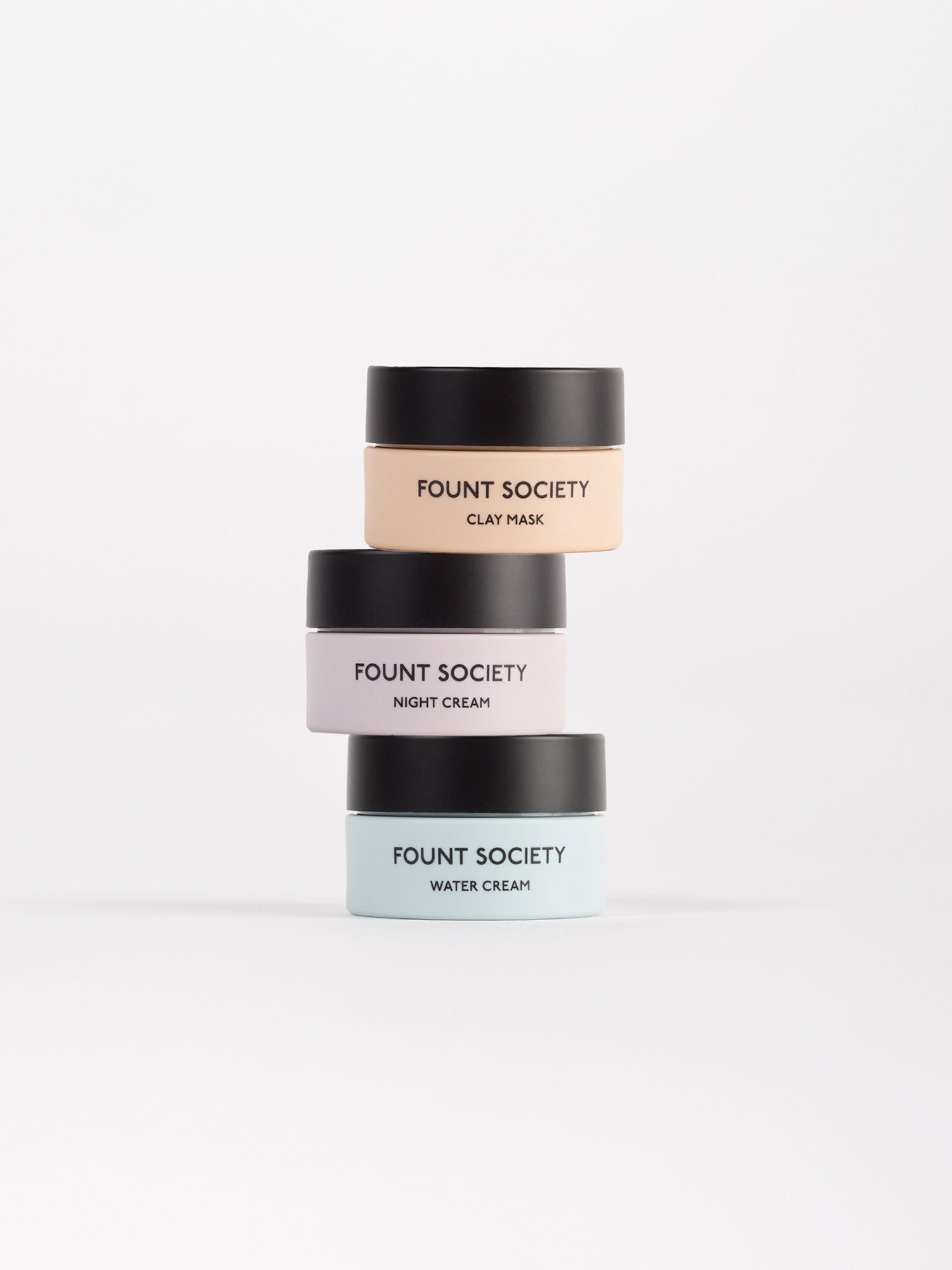 The Mini Moisture Reset Trio by Cozy Earth features three stacked skincare jars: a top peach jar labeled Clay Mask, a middle white jar labeled Night Cream, and a bottom light blue jar labeled Water Cream, all set against a plain background.