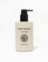 A pump bottle of "Cozy Earth Oil Cleanser" is shown. The bottle is a sleek, ivory-colored container with a black pump dispenser. The minimalist label on the front contains the brand name, product name, and volume of 148 ml (5 fl oz) along with a decorative logo.