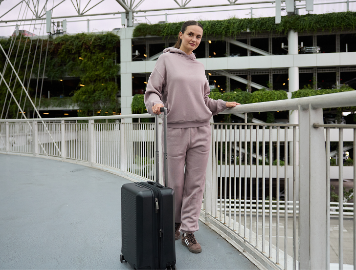 Woman in a pink tracksuit pulling a black suitcase on a bridge