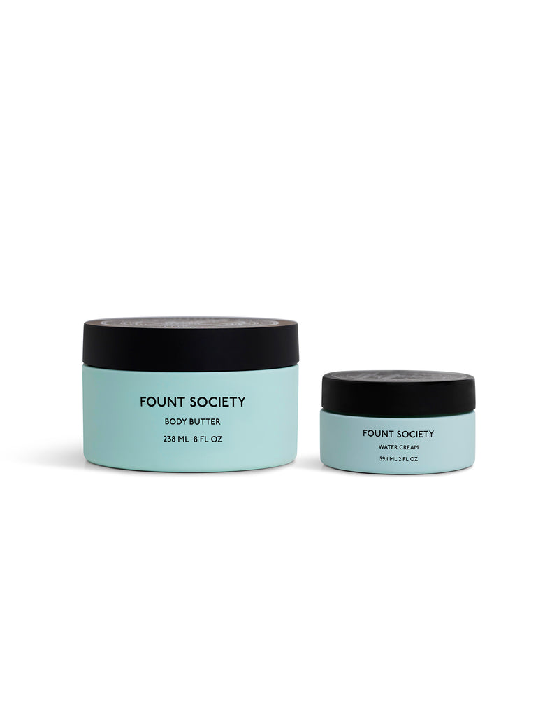 Two light blue jars with black lids from Cozy Earth, called the Dewy Duo. The larger jar is labeled Body Butter and the smaller Water Cream. Both feature a minimalistic, modern design.