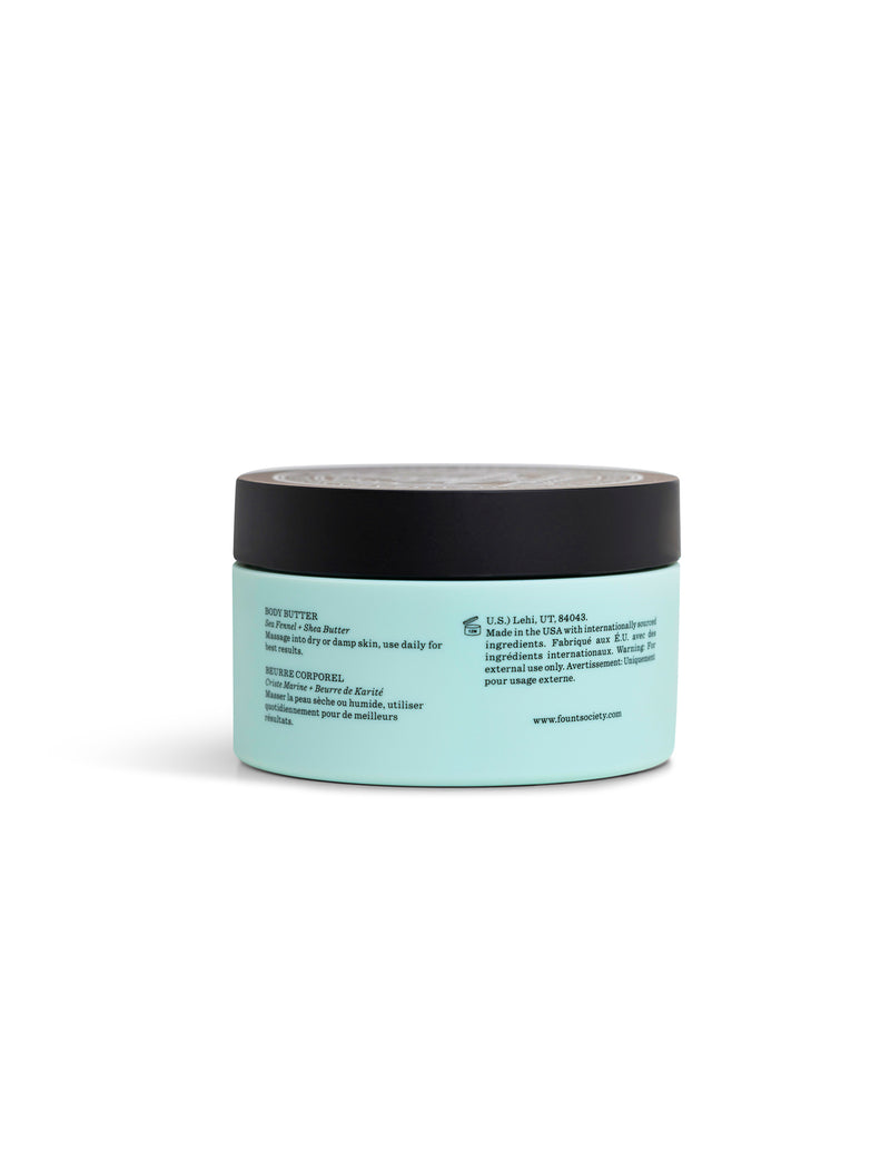 A light blue Cozy Earth Body Butter jar with a black lid displays English and French directions and product info on the label. The jar is set against a white background.