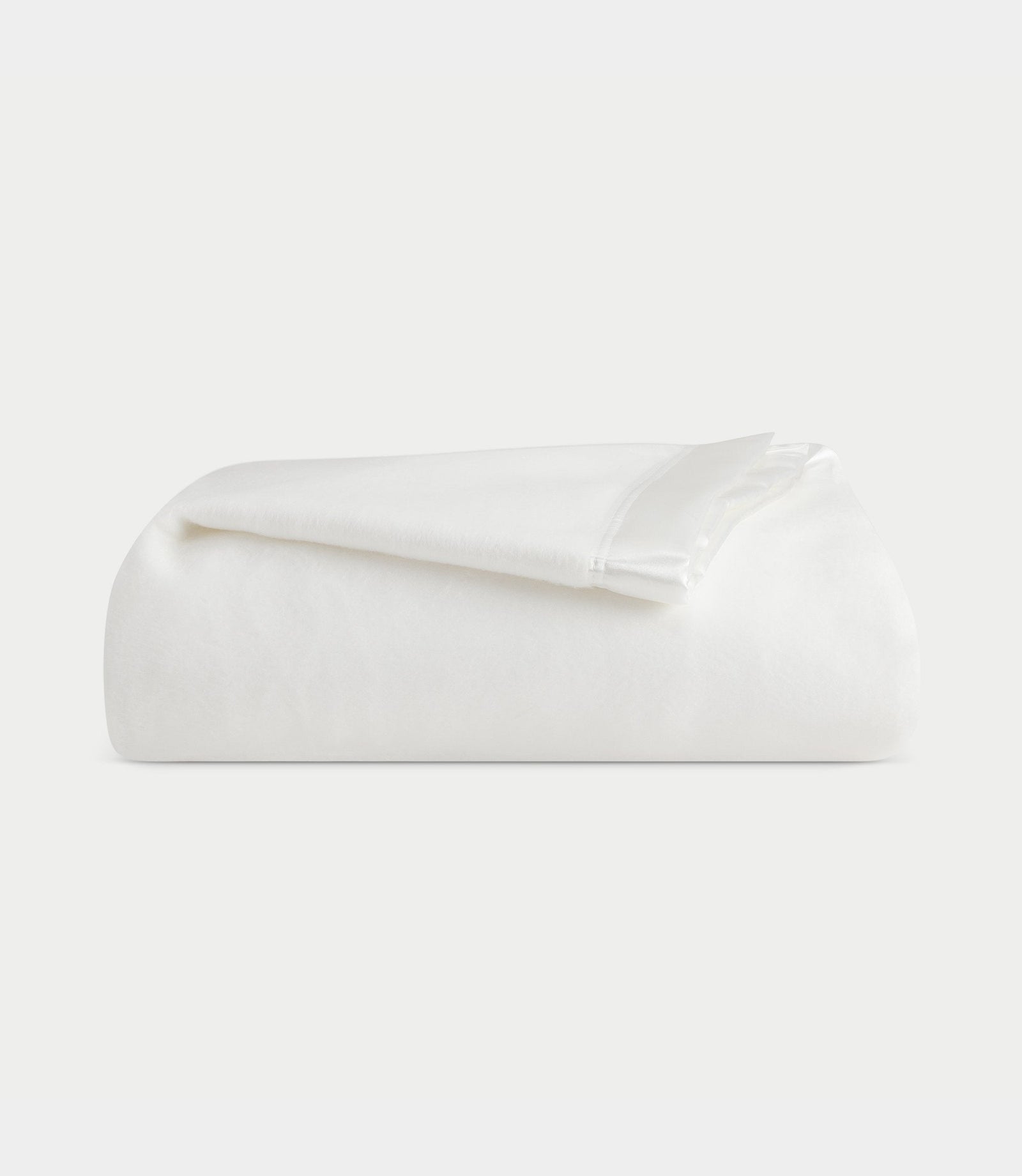 A neatly folded Bamboo Blanket from Cozy Earth is placed against a plain, light-colored background. The material appears soft and smooth, with a slightly glossy finish on the folded edges. 