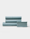 A neatly folded Bamboo Bedding Core Bundle by Cozy Earth is arranged on a plain white background, with larger pieces stacked to the left and smaller pieces to the right.|Color:River