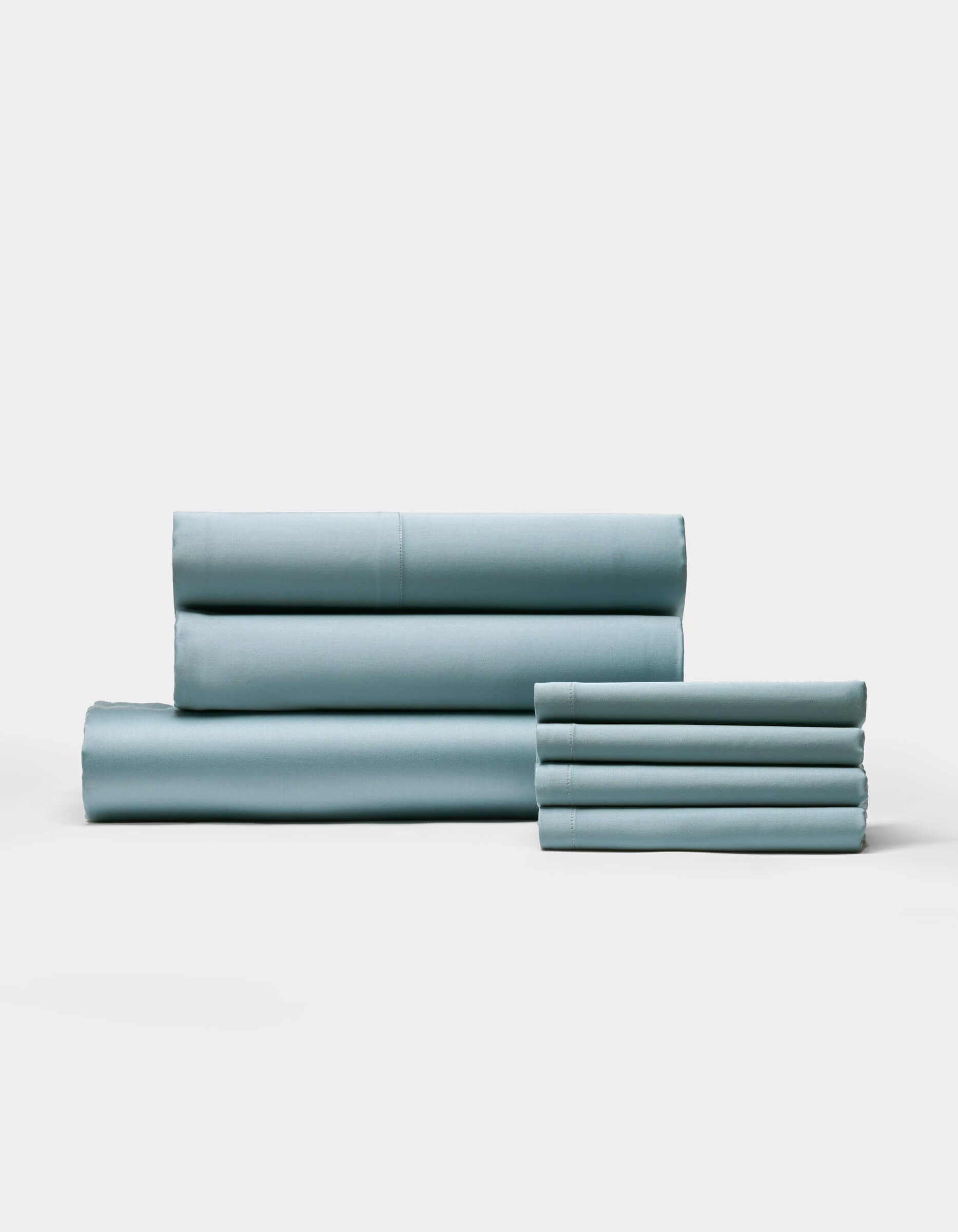 A neatly folded Bamboo Bedding Core Bundle by Cozy Earth is arranged on a plain white background, with larger pieces stacked to the left and smaller pieces to the right.|Color:River