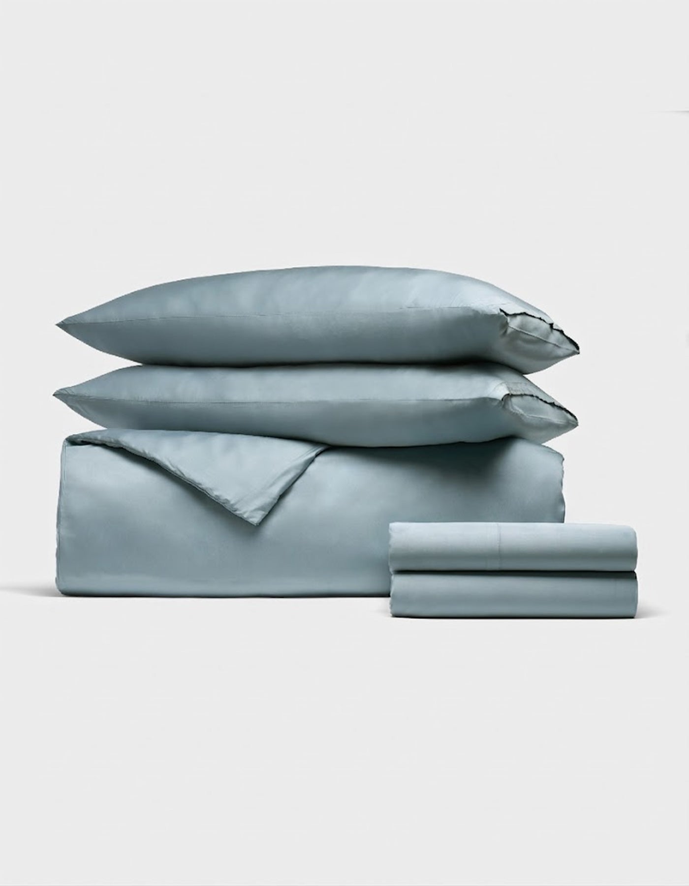 The Bamboo Bedding Deluxe Bundle by Cozy Earth features a neatly folded light blue set—including two pillows, a duvet cover, and sheets—elegantly displayed against a plain white background.