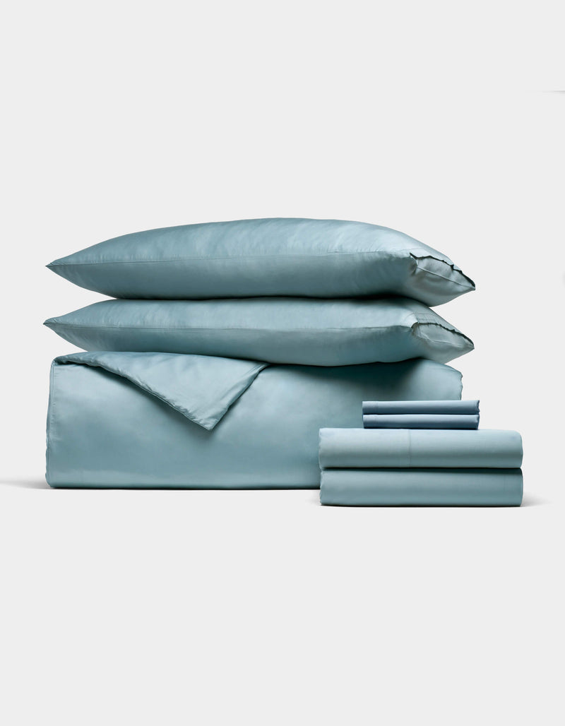 The Cozy Earth Bamboo Bedding Ultimate Bundle, featuring a light blue duvet cover, two pillows, and neatly folded sheets, is displayed against a white background.