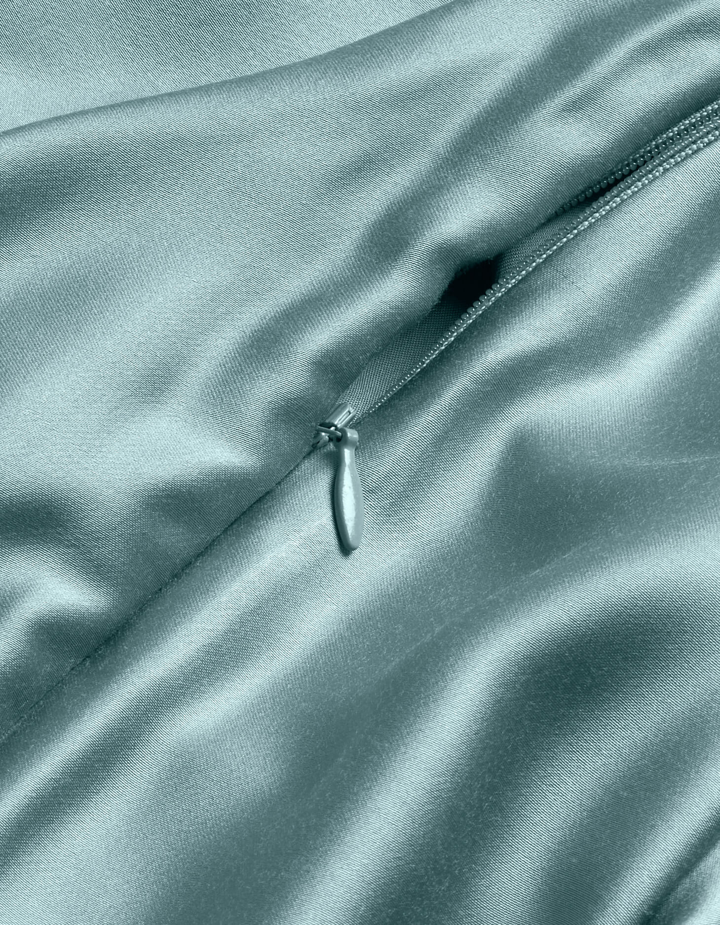 A close-up of the Cozy Earth Bamboo Duvet Cover in light blue shows its shiny, delicate satin texture with a partially unzipped zipper highlighting the smooth, luxurious folds.