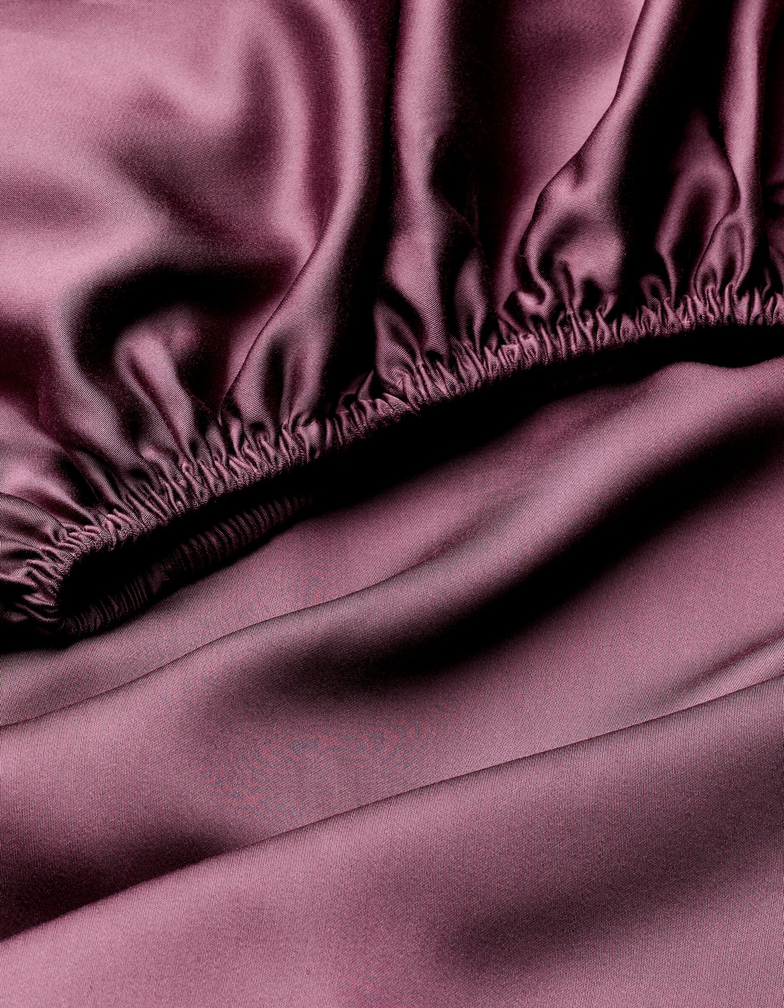 Close-up of Cozy Earth Bamboo Sheet Set showing mauve satin fabric with gentle folds and gathered elastic stitching along the edge, giving a smooth and glossy texture.