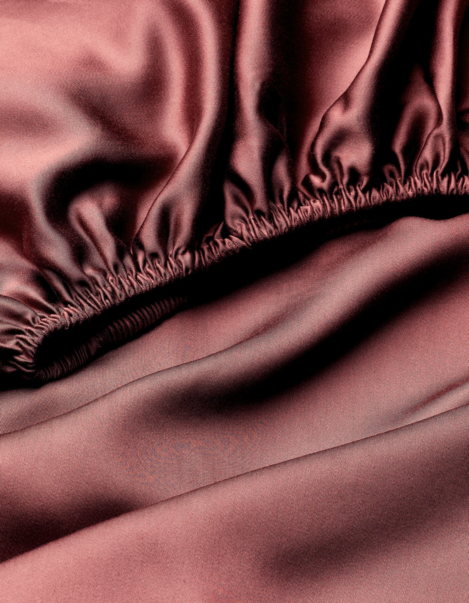 Close-up of Cozy Earth's Bamboo Fitted Sheet in smooth, silky dark pink fabric with gathered elastic edge and a shiny, luxurious finish.
