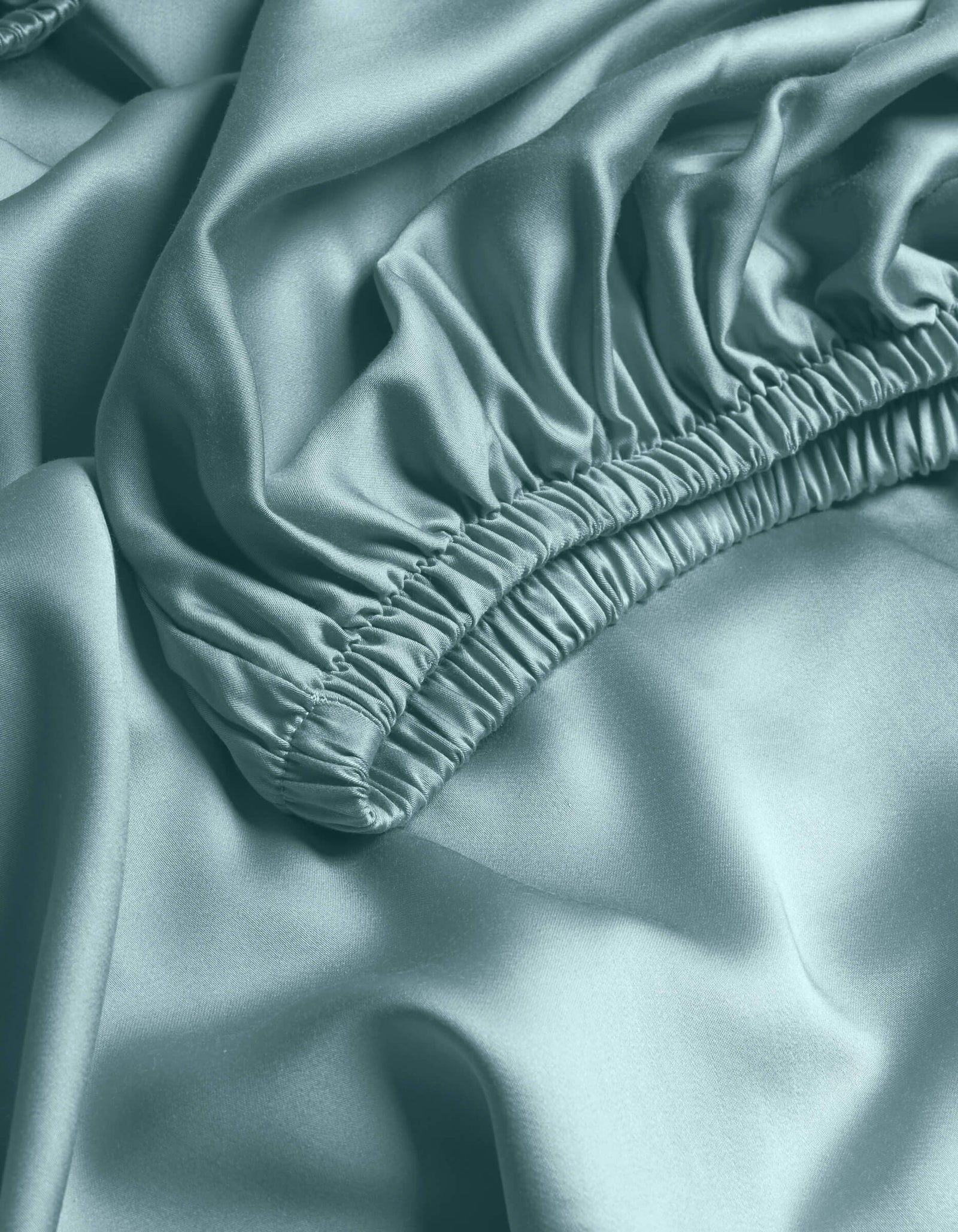 Close-up of Cozy Earth's Bamboo Fitted Sheet in light blue, featuring gathered elastic edges and a smooth, shiny texture with soft folds.