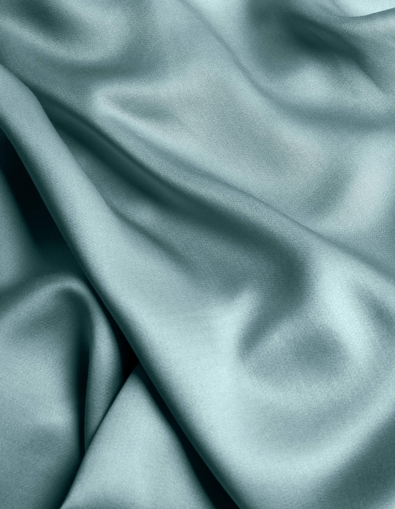 The Cozy Earth Bamboo Sheet Set features smooth, light blue satin fabric with gentle folds and a soft, flowing texture for a shiny, elegant look.