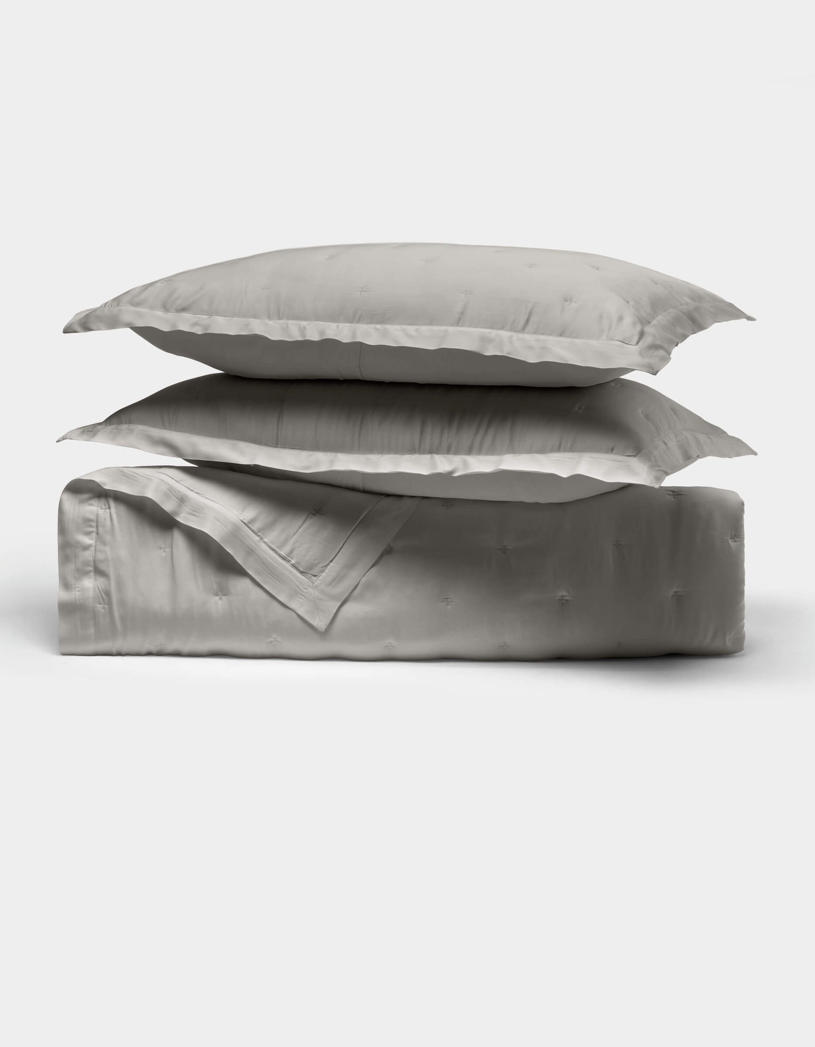 The Cozy Earth Bamboo Quilt Bundle features two light gray pillows stacked atop a folded matching comforter, all crafted from smooth, shiny fabric, displayed against a plain white background.