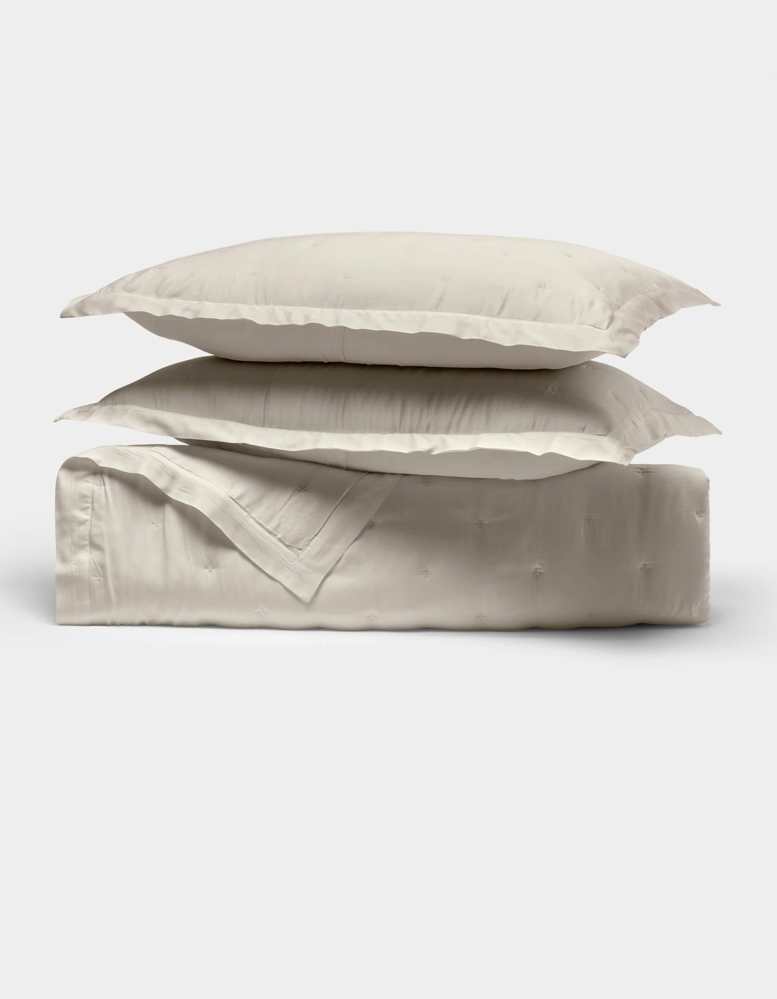 Two cream-colored pillows from Cozy Earth's Bamboo Quilt Bundle are stacked atop a neatly folded matching quilt, all displayed against a plain white background.