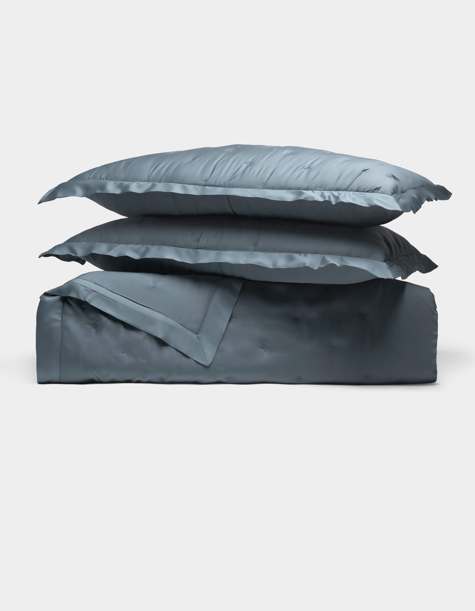Two Cozy Earth Bamboo Quilt Bundle blue satin pillows are stacked atop a matching folded comforter, all set against a plain white background.