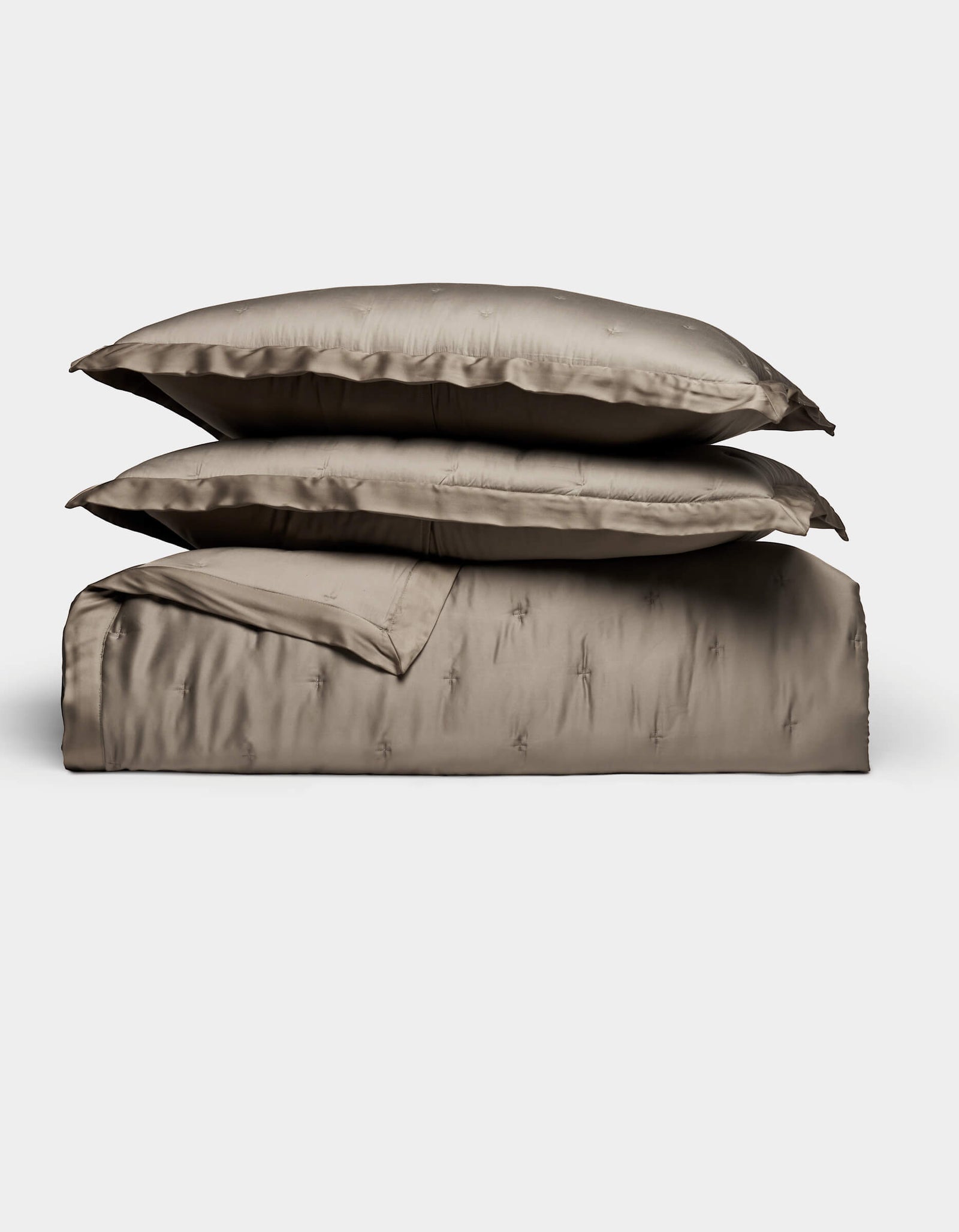 The Cozy Earth Bamboo Quilt Bundle features two plush pillows and a folded, shiny taupe duvet, all neatly arranged against a plain white background.