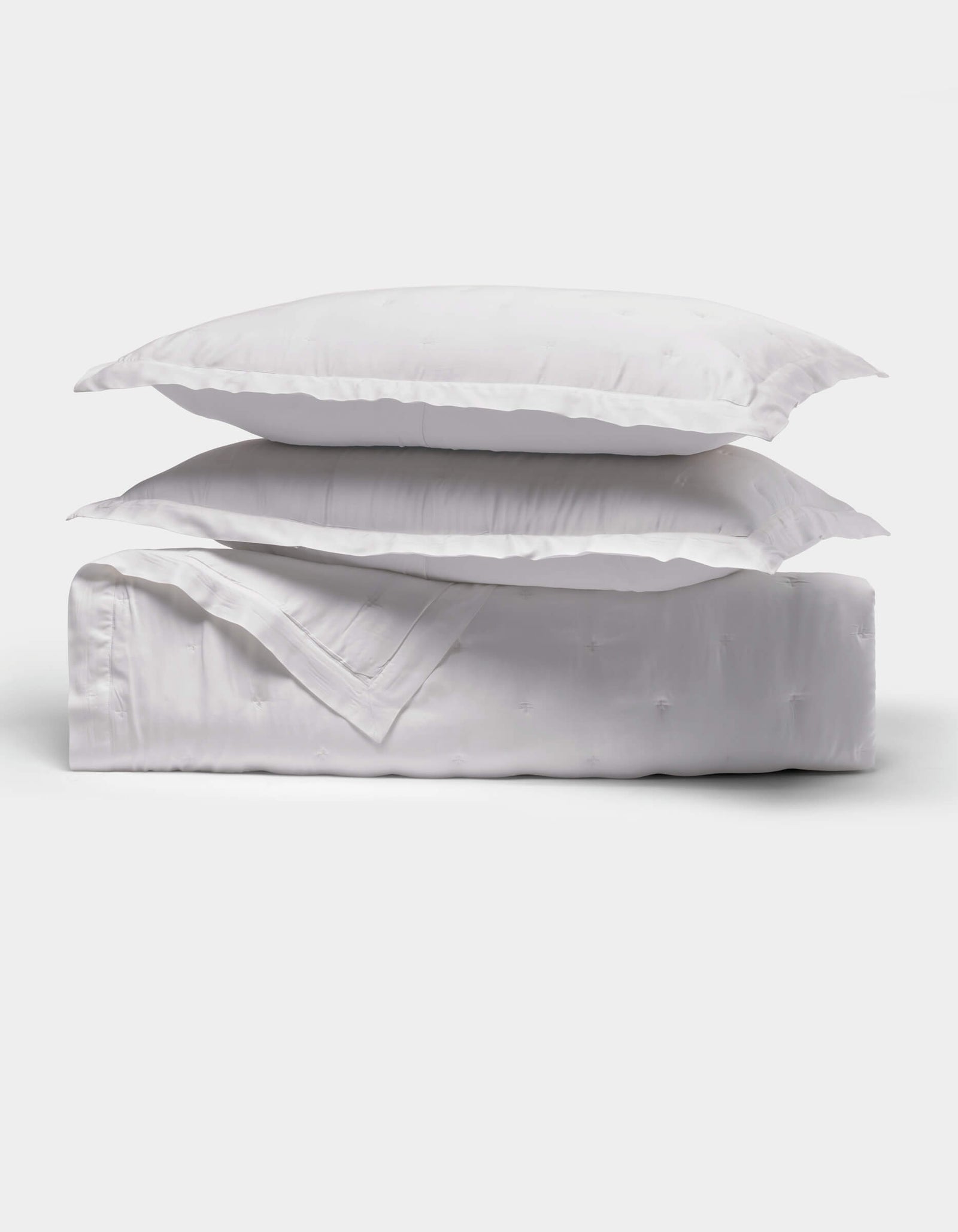 The Cozy Earth Bamboo Quilt Bundle features two fluffy white pillows stacked on a neatly folded white comforter, all shown against a plain white background.
