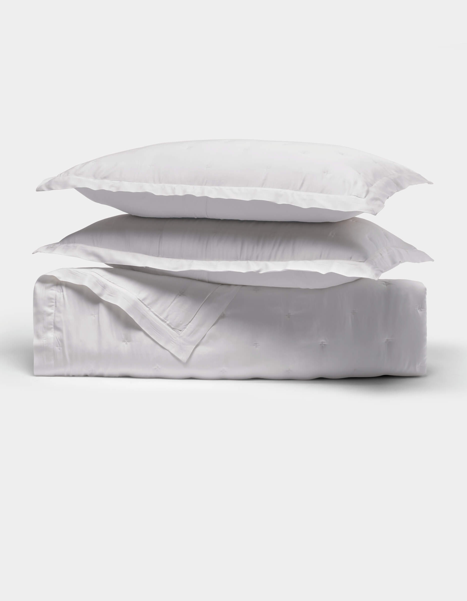 The Cozy Earth Bamboo Quilt Bundle features two fluffy white pillows stacked on a neatly folded white comforter, all shown against a plain white background.|Color:White