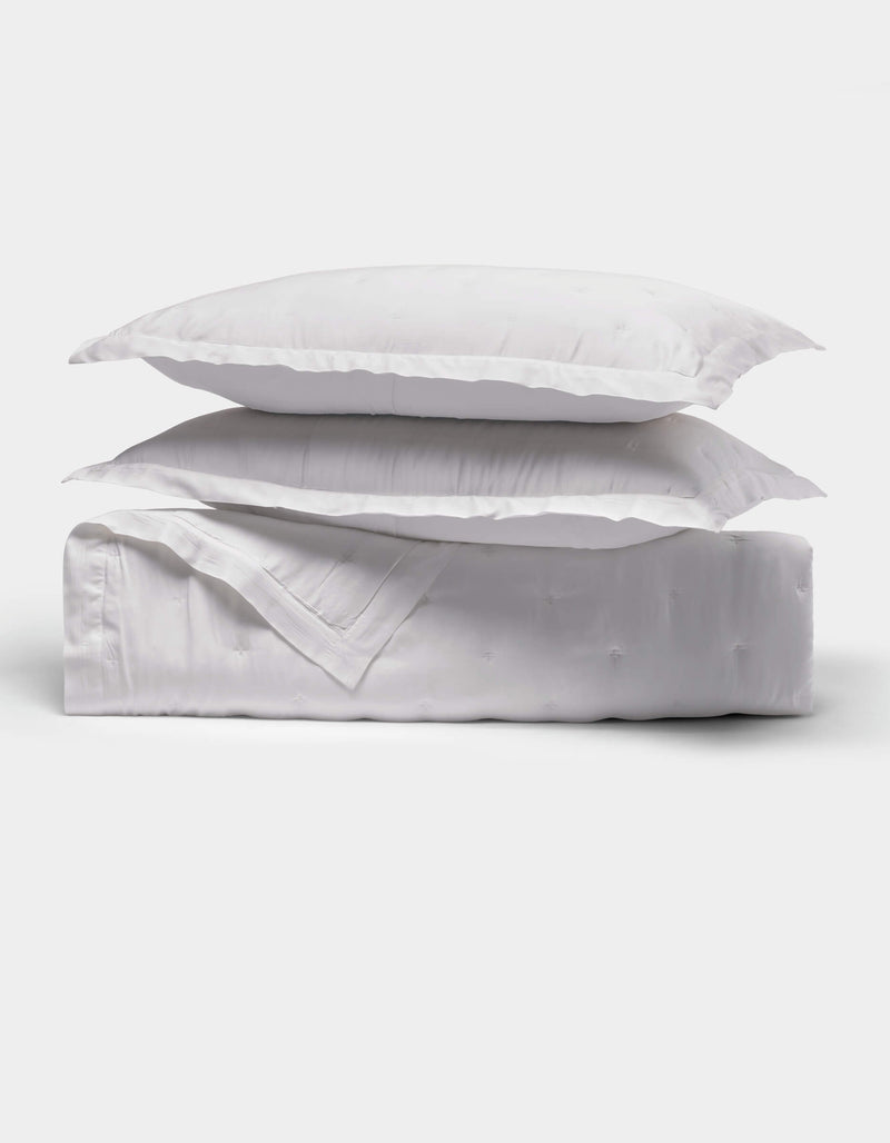 The Cozy Earth Bamboo Quilt Bundle features two fluffy white pillows stacked on a neatly folded white comforter, all shown against a plain white background.