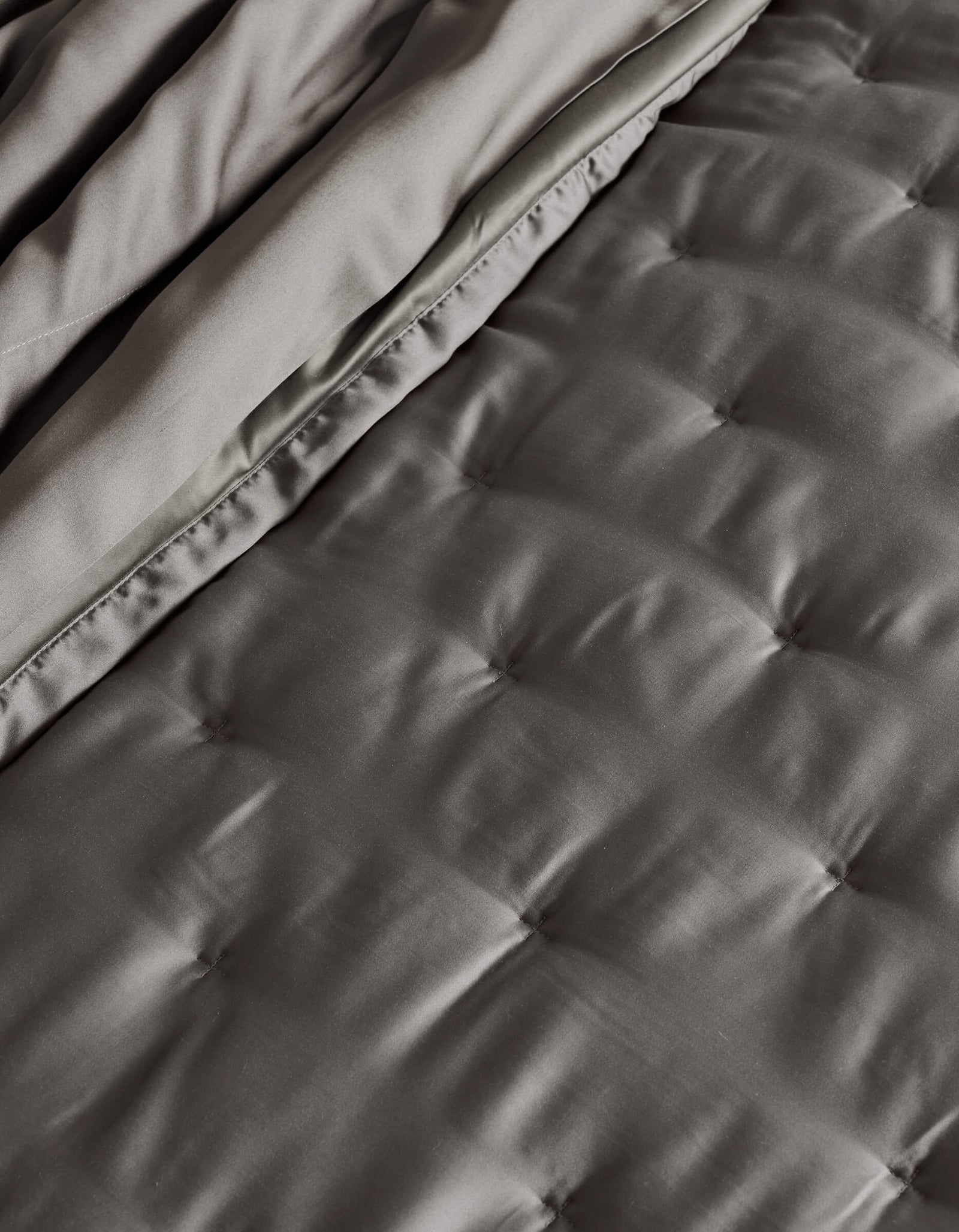 A close-up of the Cozy Earth Bamboo Quilt, neatly folded, showcasing its quilted dark gray design with smooth, satin-like texture and square stitching.