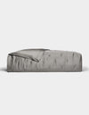 A neatly made bed features the Cozy Earth Bamboo Quilt in smooth, shiny silver-gray satin, partially folded back at the top, set against a plain white background.|Color:Charcoal